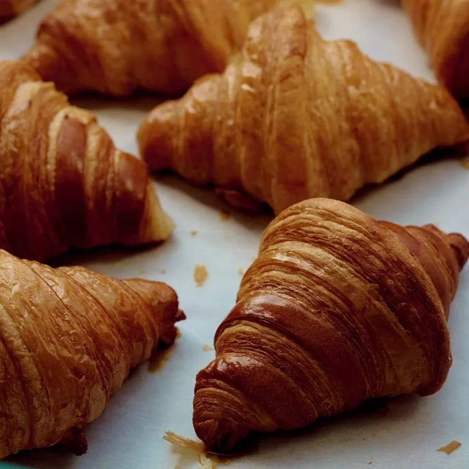 Several golden-brown croissants on white parchment paper.