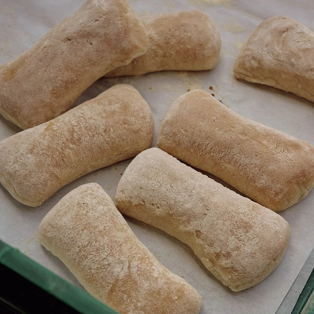 Uncooked bread rolls dusted with flour on a baking sheet lined with parchment paper.