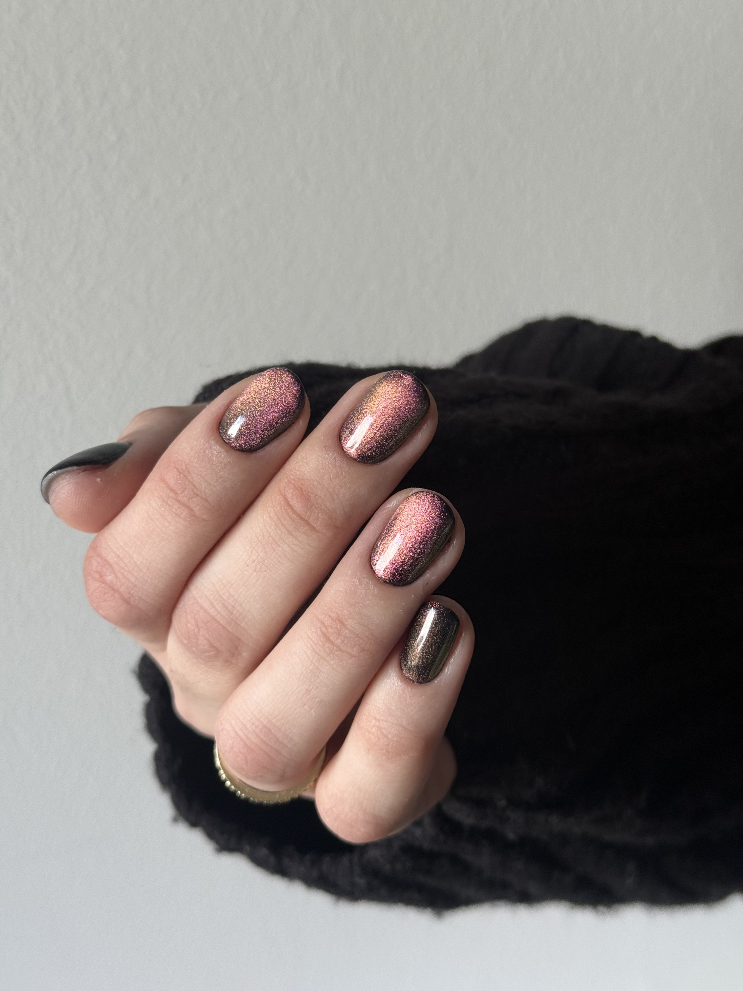Person's hand with metallic, glittery, multicolored nail polish against a plain light background.