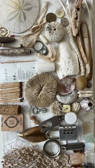 Collection of seashells, buttons, a padlock, a cork, a spoon, a magnifying glass, a tube, a paper, and other small objects arranged on a surface.