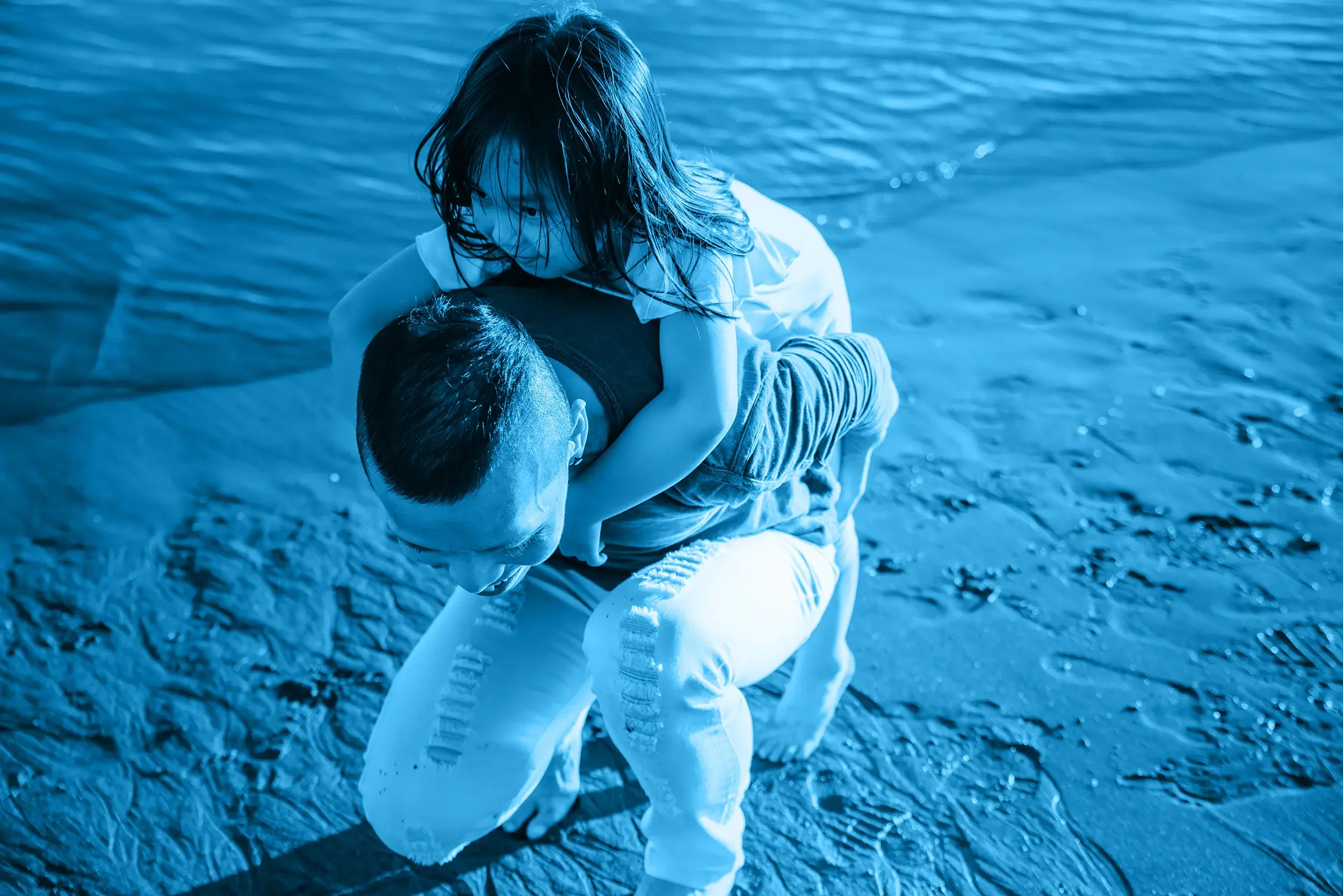 A girl with wet hair playing on a sandy beach with her dad during daytime.