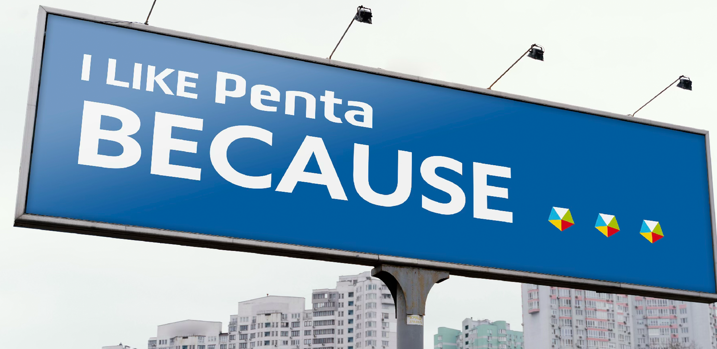 Blue billboard with white text that reads 'I LIKE Penta BECAUSE' with three colorful small umbrellas or beach toys below the text, city buildings in the background, and a cloudy sky.