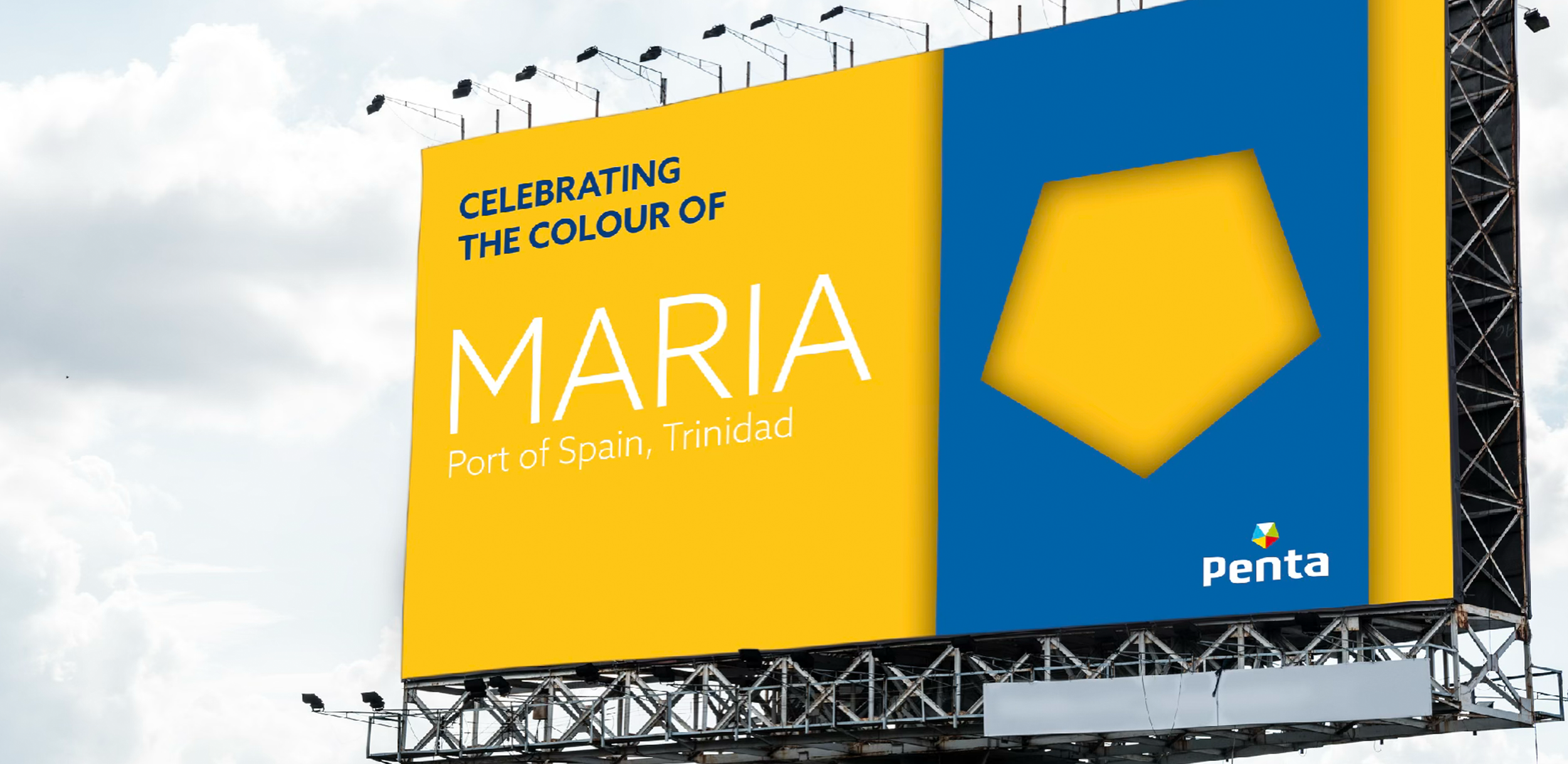 Billboard celebrating the color yellow, featuring the text "Celebrating the Colour of Maria, Port of Spain, Trinidad" with the Penta logo at the bottom, set against a partly cloudy sky.