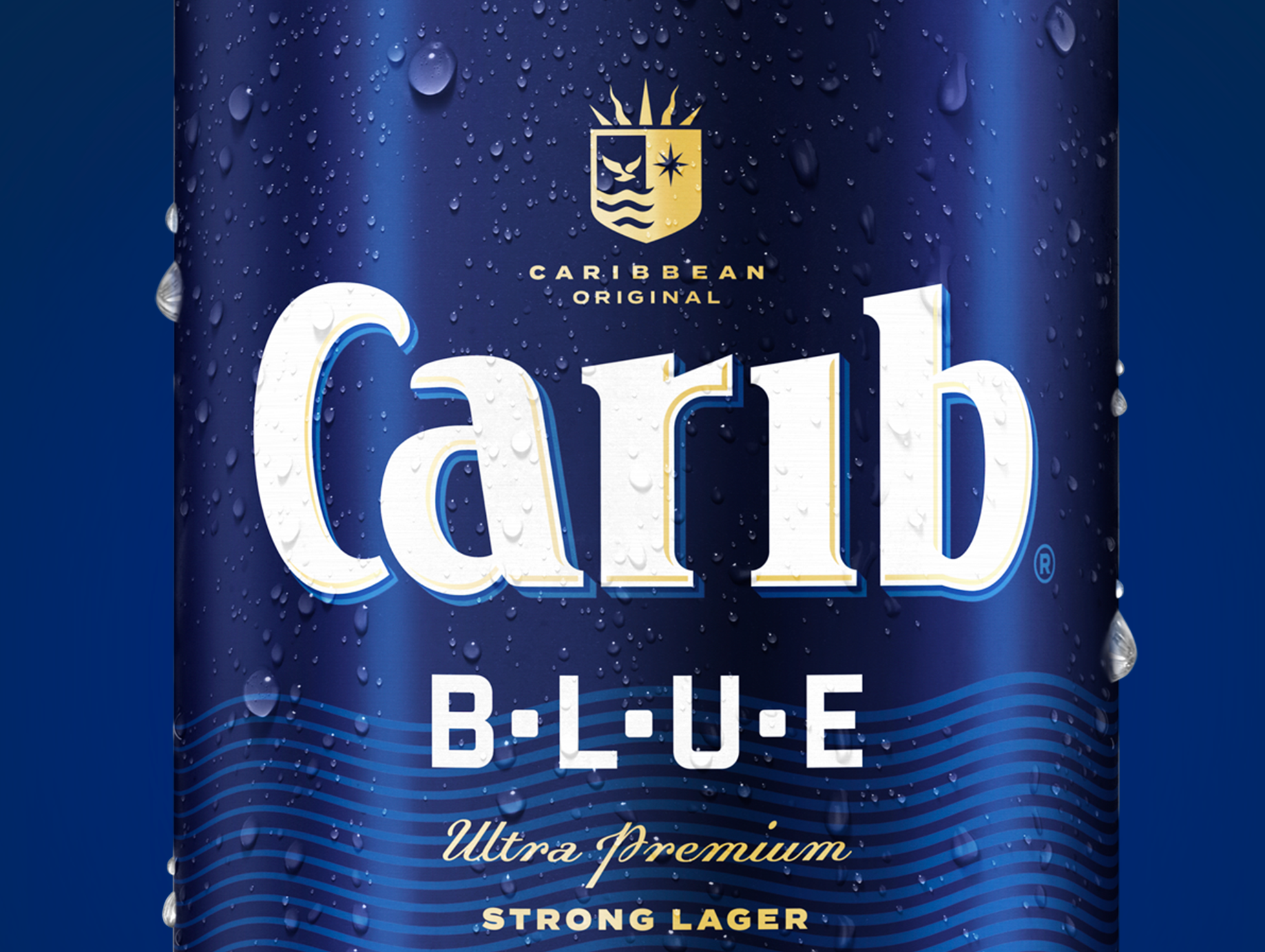 Close-up of a blue beer can with water droplets, featuring the Carib Blue logo, a crest with a sun, a star, and waves, indicating Caribbean origin. The text on the can reads "Carib Blue," "Ultra Premium," and "Strong Lager."