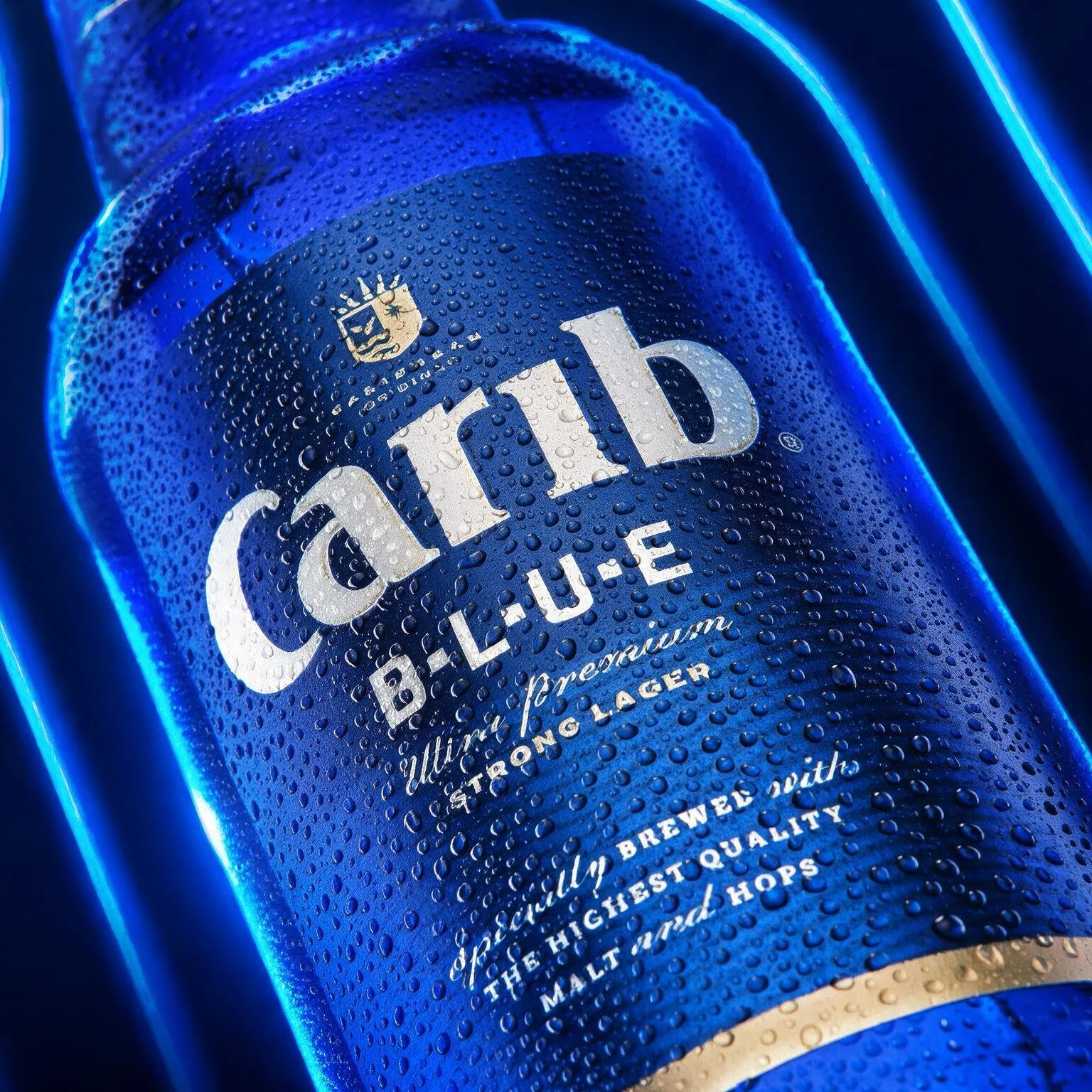 Close-up of Carib Blue beer bottle with condensation, digital blue lighting, and the brand's logo and text visible.