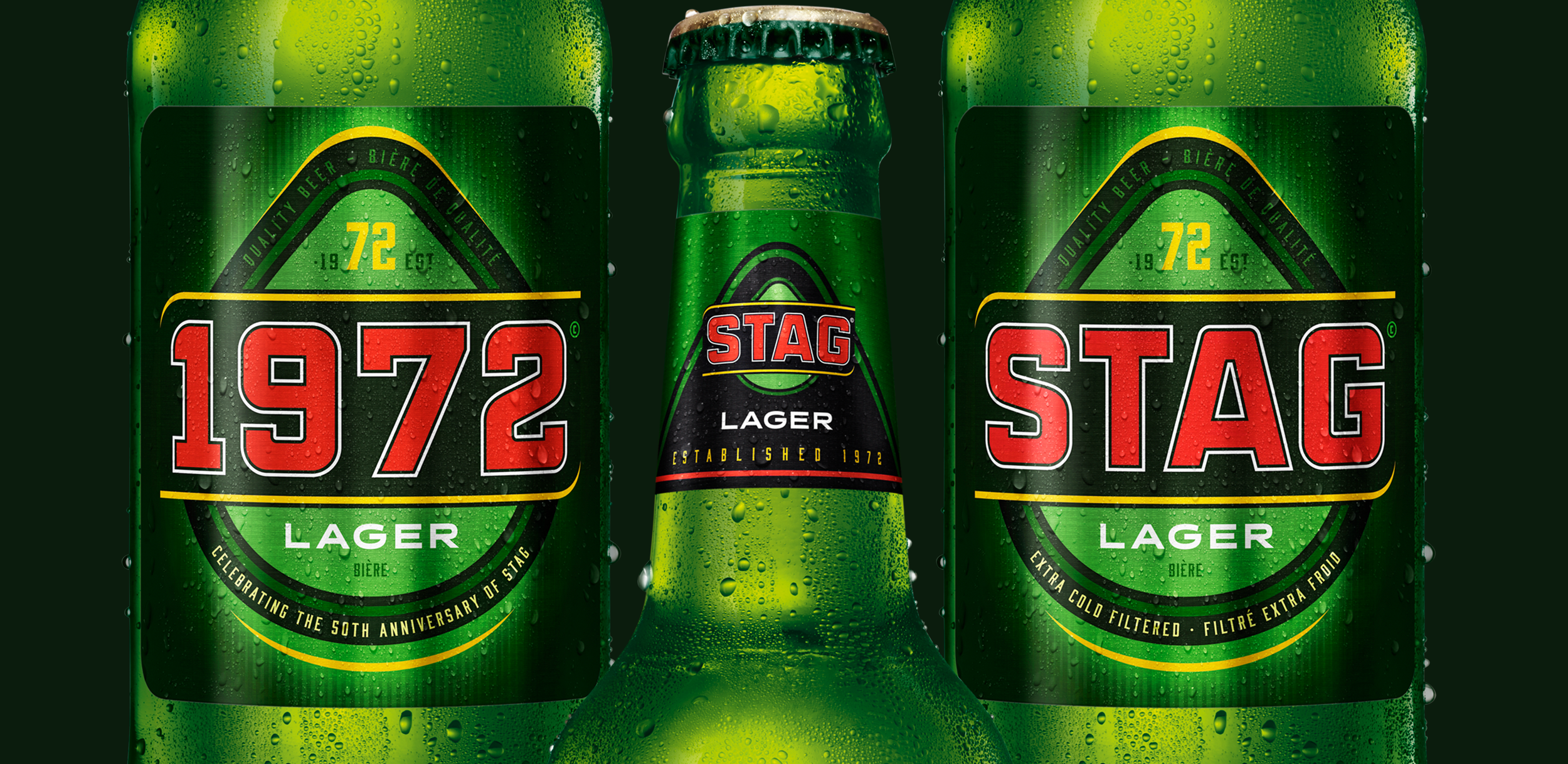Close-up of three bottles of Stag Lager with water droplets on the surface, featuring green labels with red, black, and yellow text.