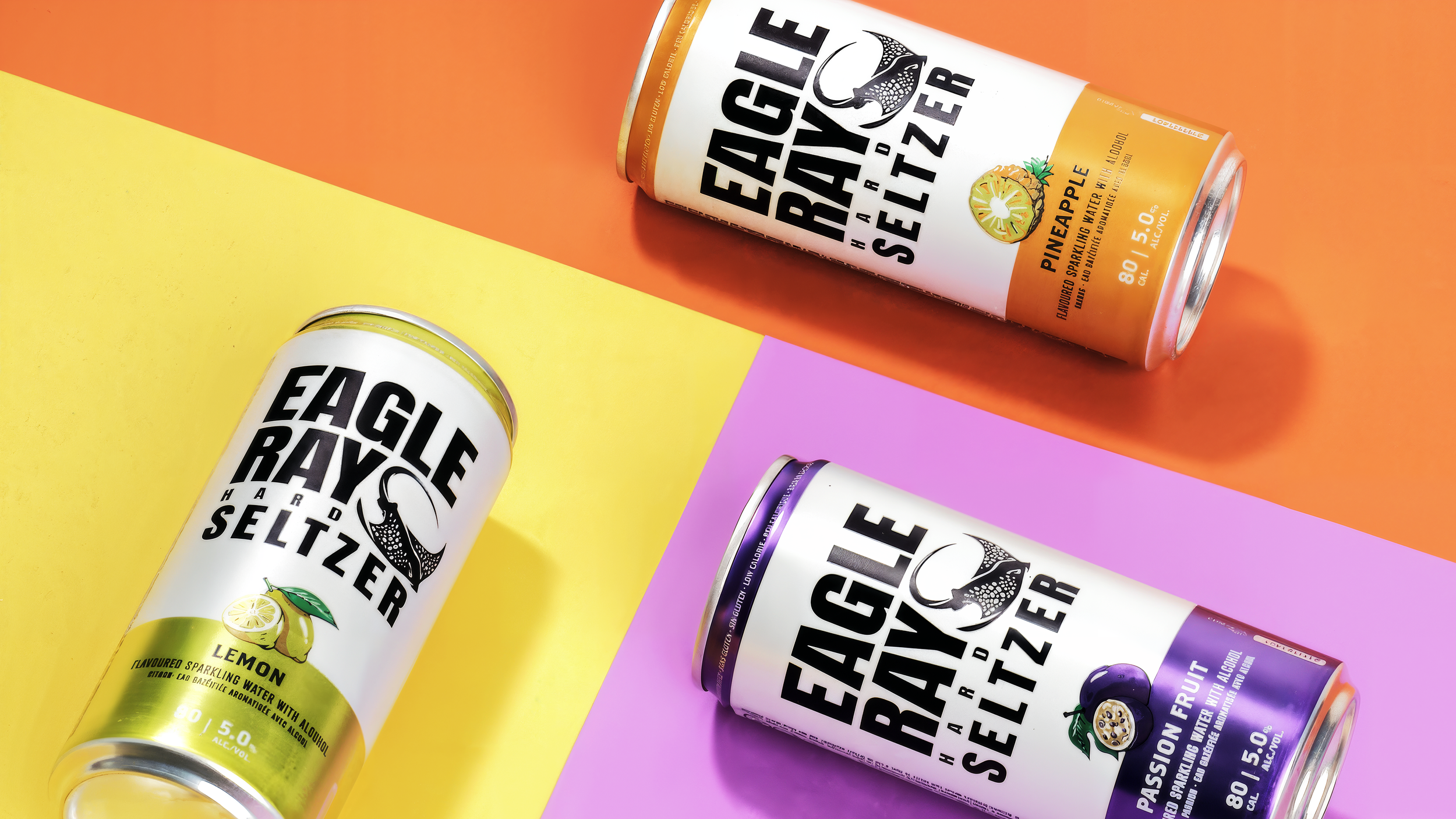 Four cans of flavored Eagle Ray Seltzer with alcohol on colorful backgrounds in yellow, pink, purple, and orange.