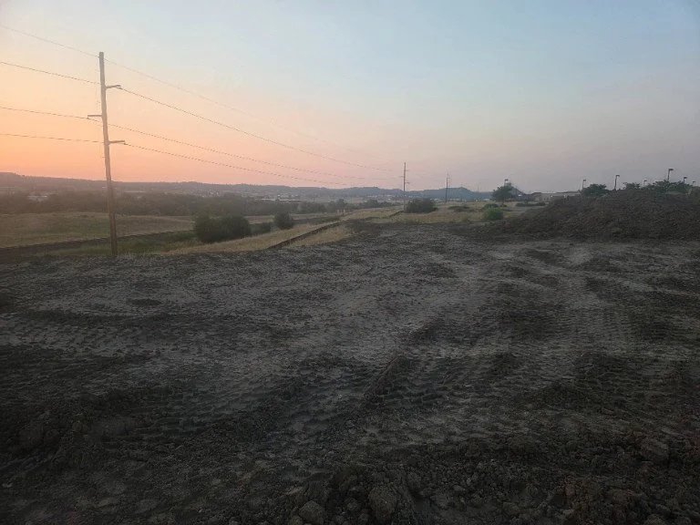Dirt road with tire tracks, utility poles, and a sunset sky over an open rural landscape.