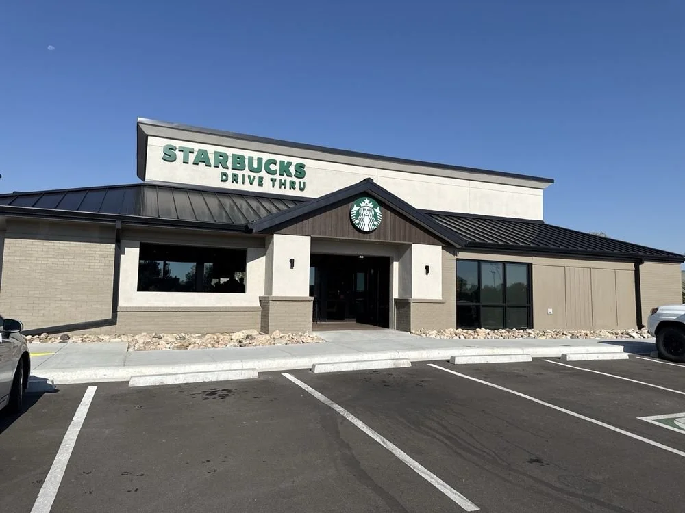 Starbucks coffee shop with a drive-thru, parking lot, and clear blue sky.