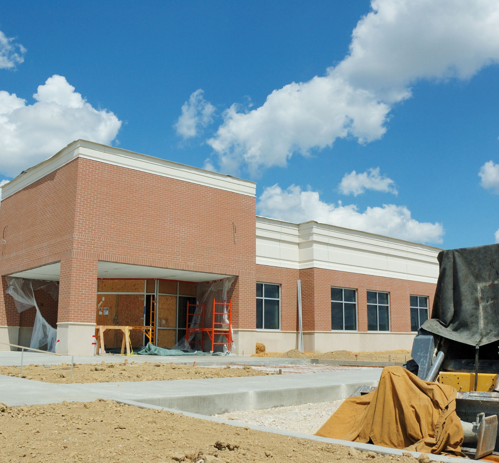 A brick commercial building under construction with large windows and a covered entrance, partly visible sky with scattered clouds.