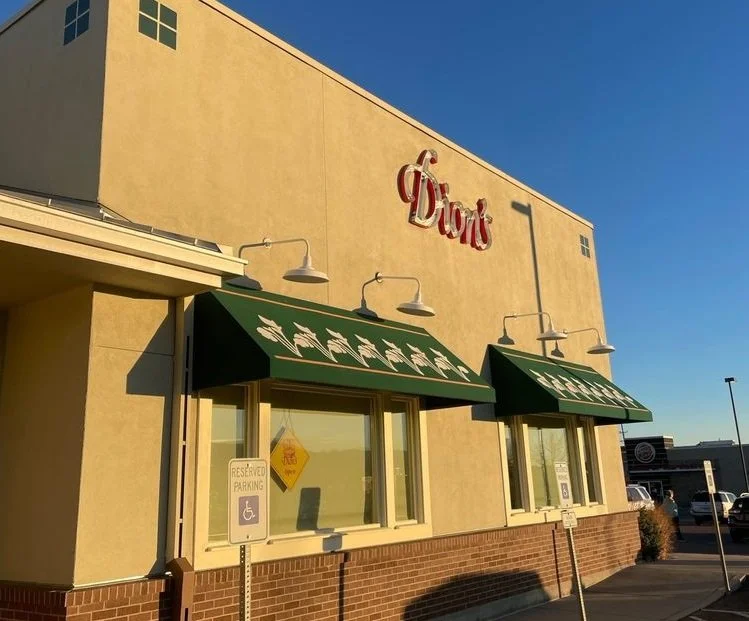 Exterior of a building with green awnings and a sign that says 'Dunkin' in red letters, with a parking lot in front.