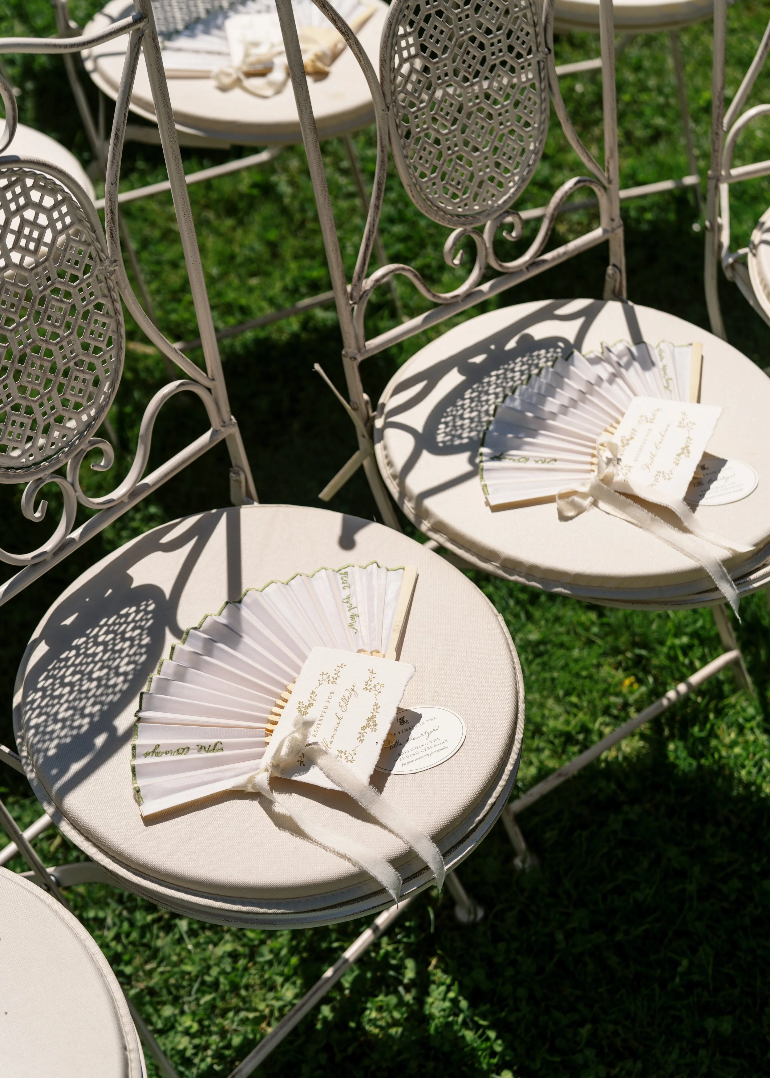 Custom paper fans and wedding details placed on ceremony chairs for an outdoor celebration.