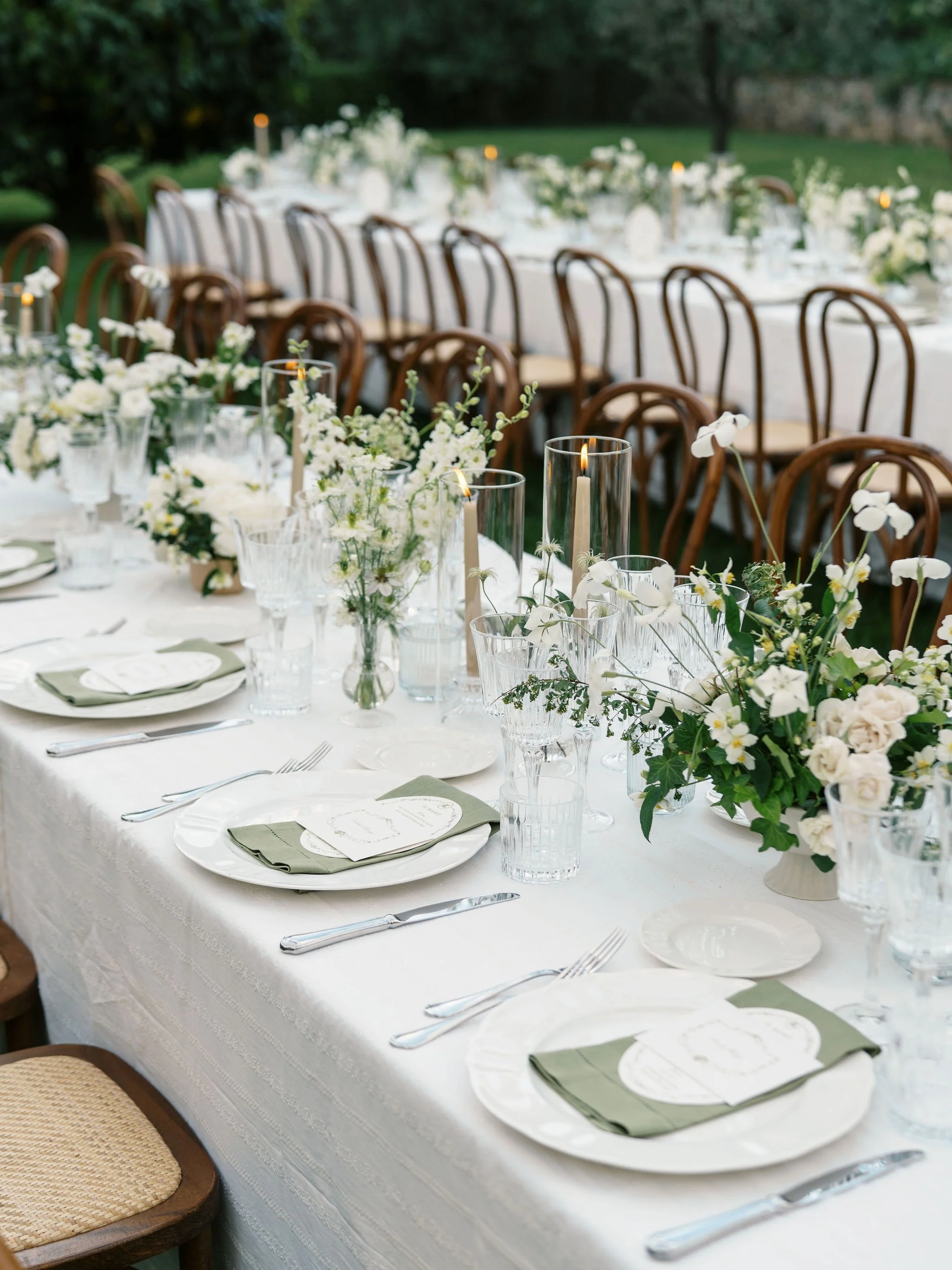Outdoor wedding reception table with custom stationery, florals, candles, and layered place settings.
