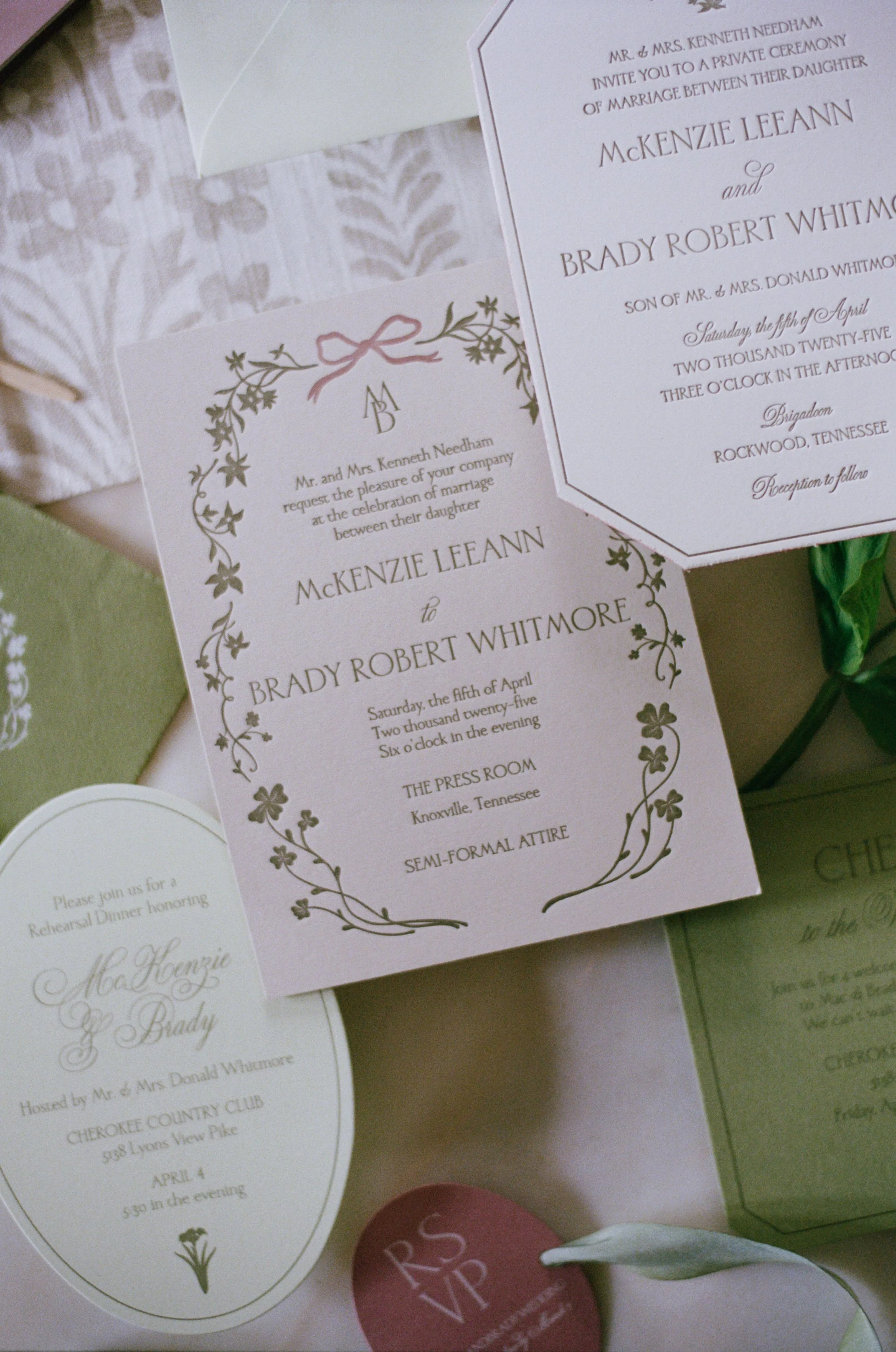 Wedding invitations and event details on decorative paper, with a white flower and green leafy accents.