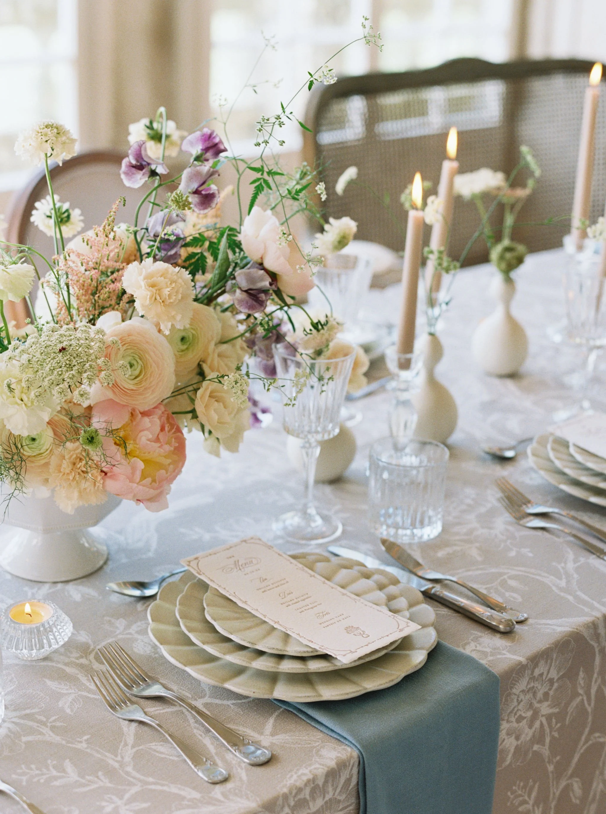 Wedding reception place setting with a custom menu, florals, candles, and layered table details.