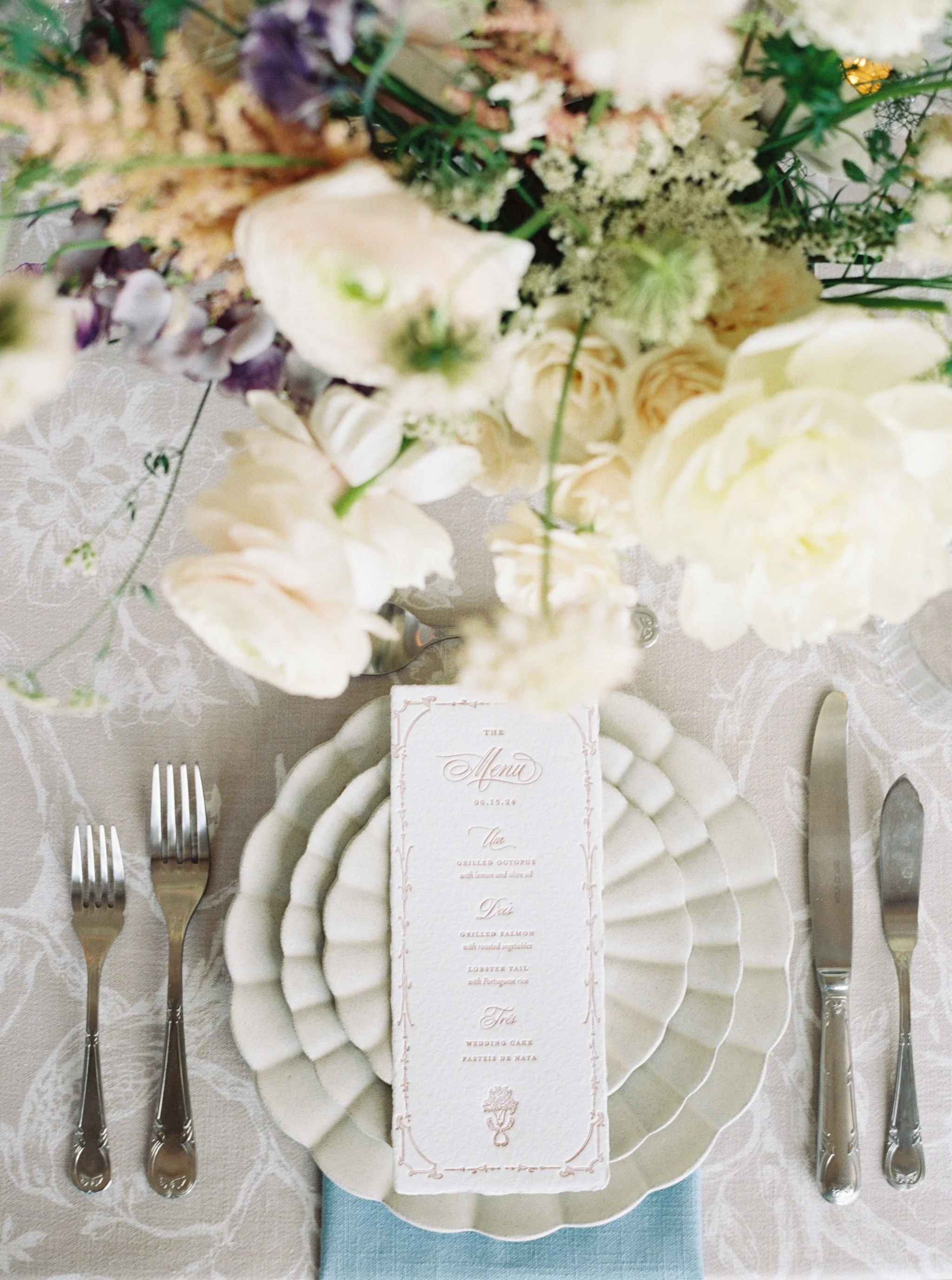 Custom wedding menu designed by Merci Studio within a romantic floral reception place setting.