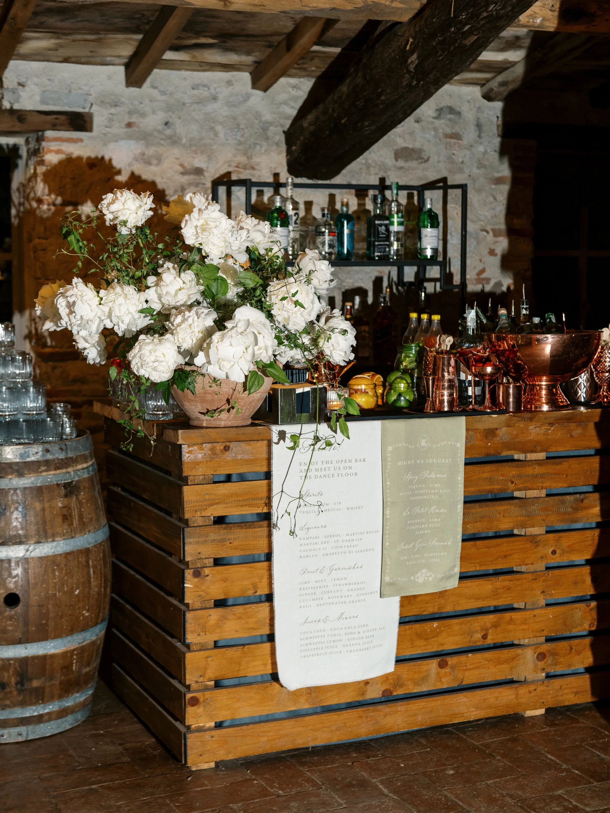 Wedding bar with custom signage, white florals, and reception details in a rustic Italian setting.