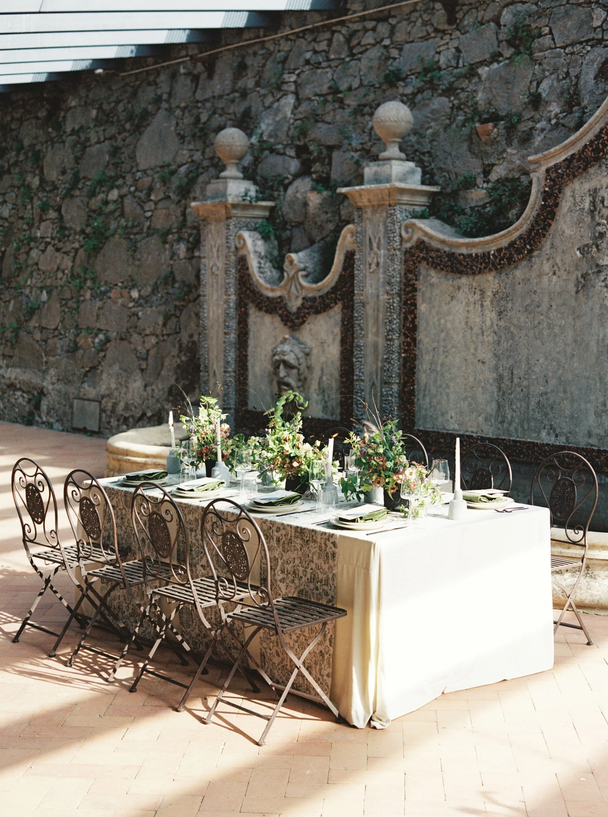 Intimate outdoor wedding reception table surrounded by historic stonework and garden details.