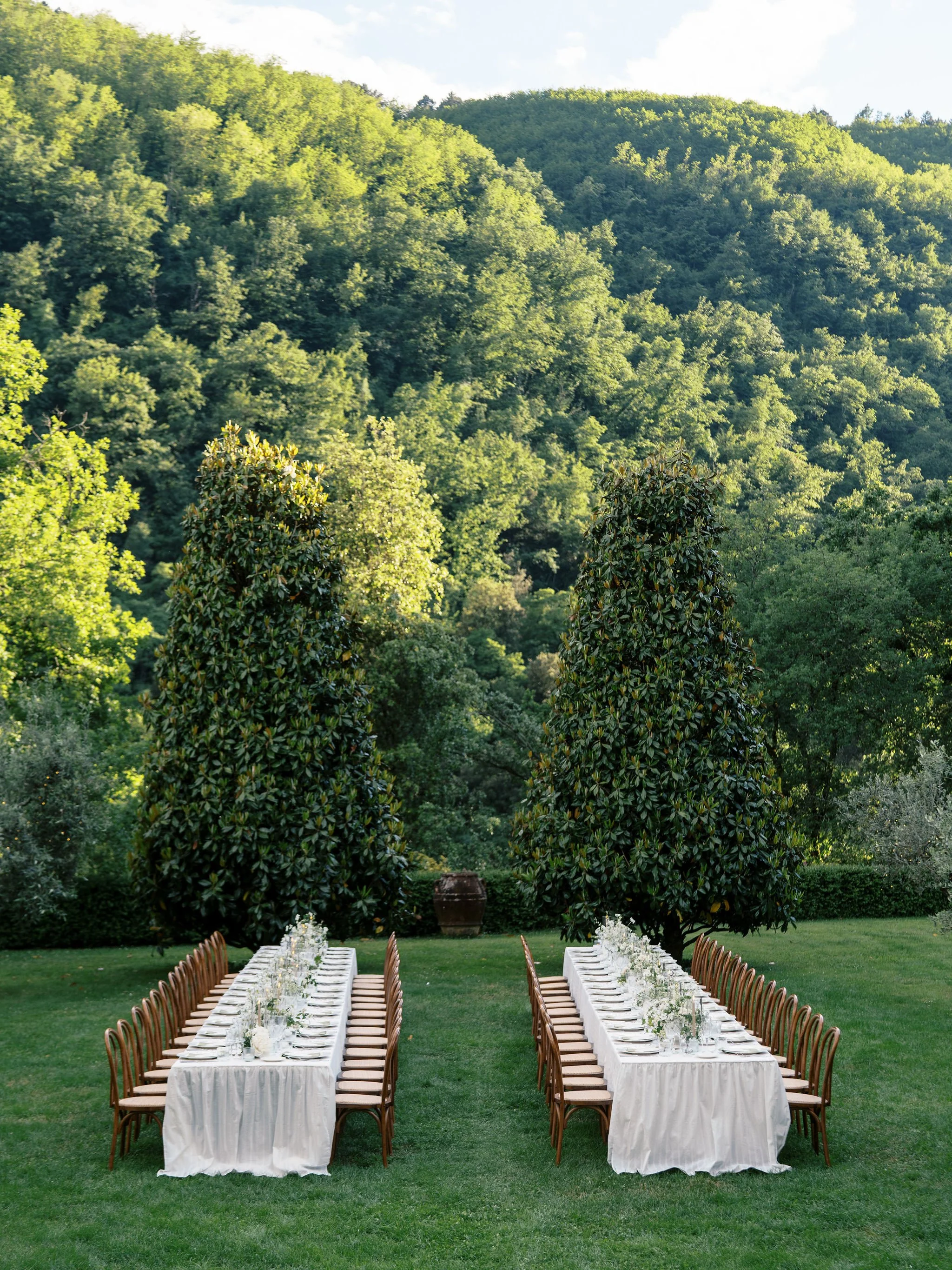 Outdoor wedding reception in the Tuscan countryside with long tables, white florals, and custom event details.