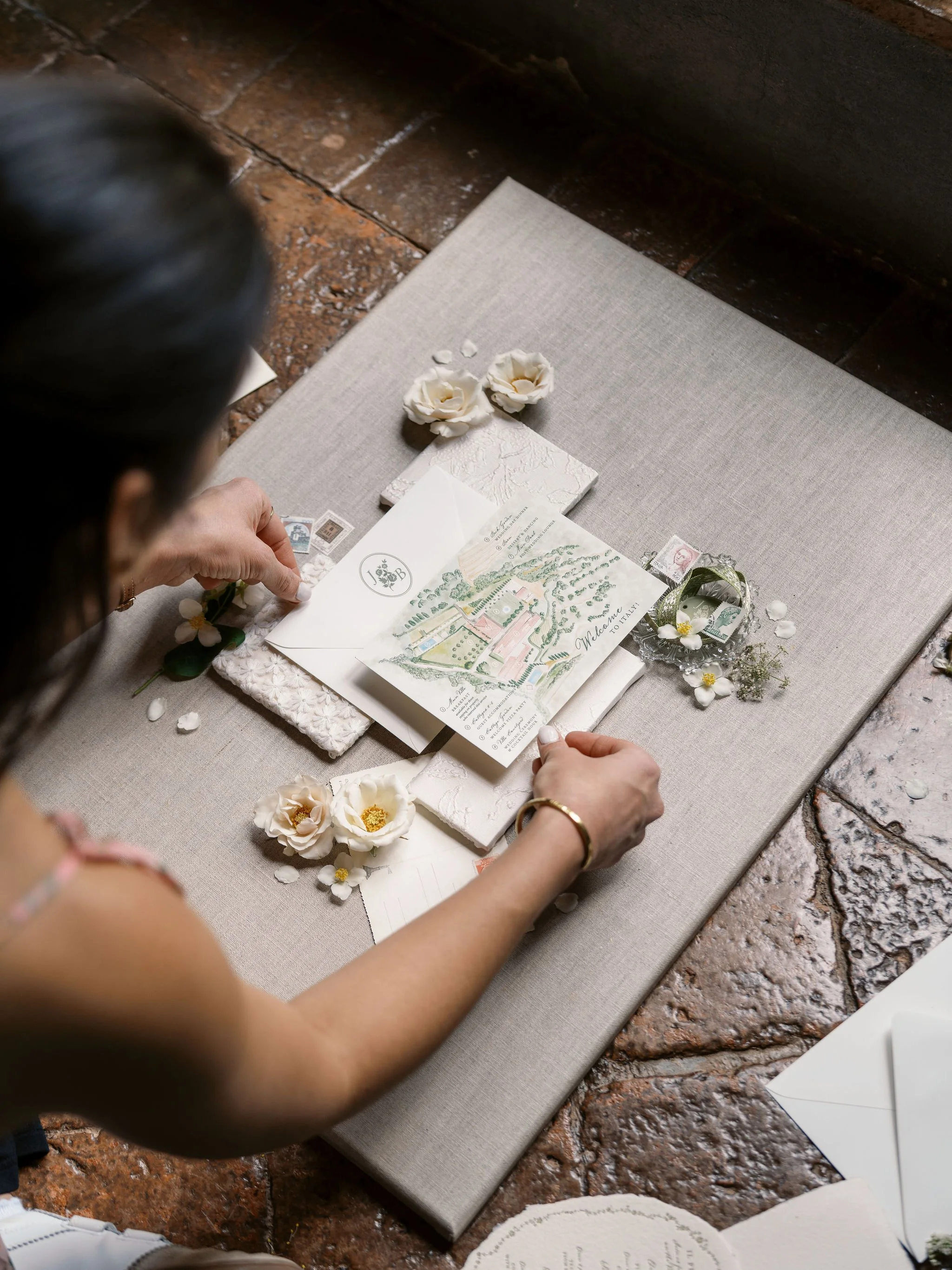 Bespoke wedding invitations and paper details being arranged with flowers and greenery.
