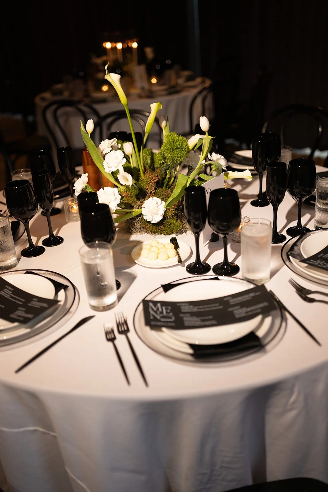Black and white wedding reception table with custom paper details, white florals, and candlelight.