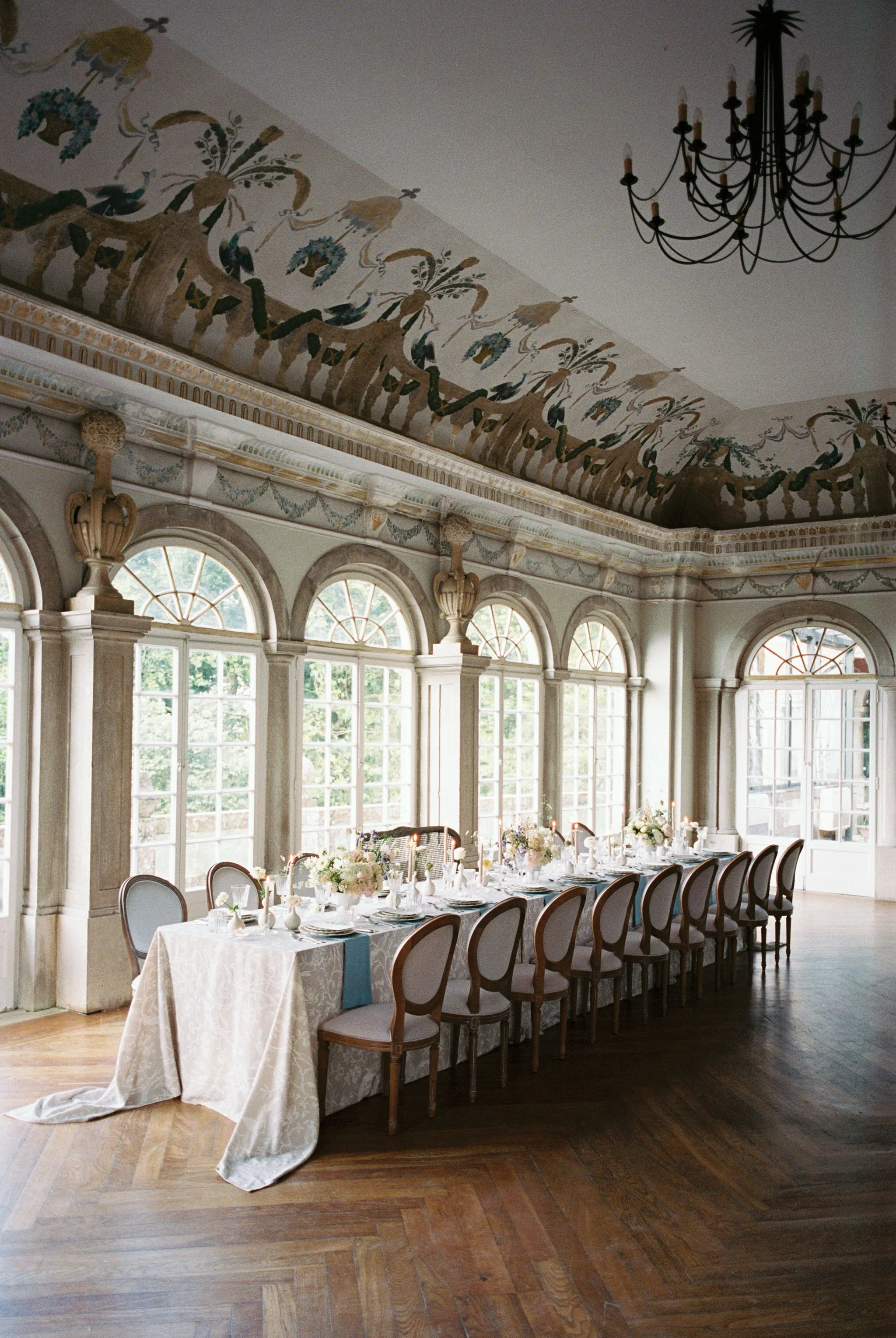 Wedding reception in a historic dining room with frescoed ceilings, florals, and a long banquet table.