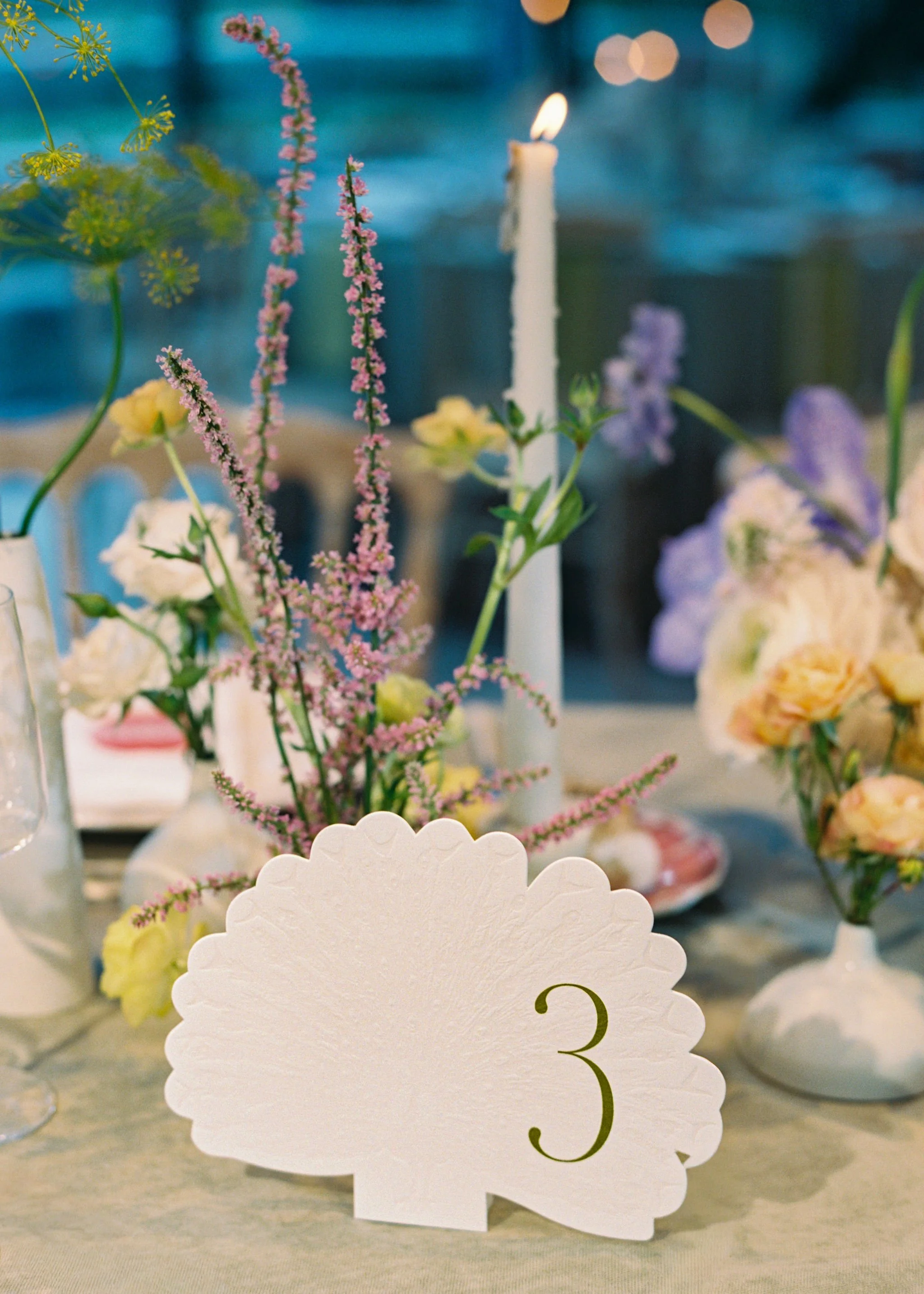 Custom wedding table number designed by Merci Studio among colorful reception florals.