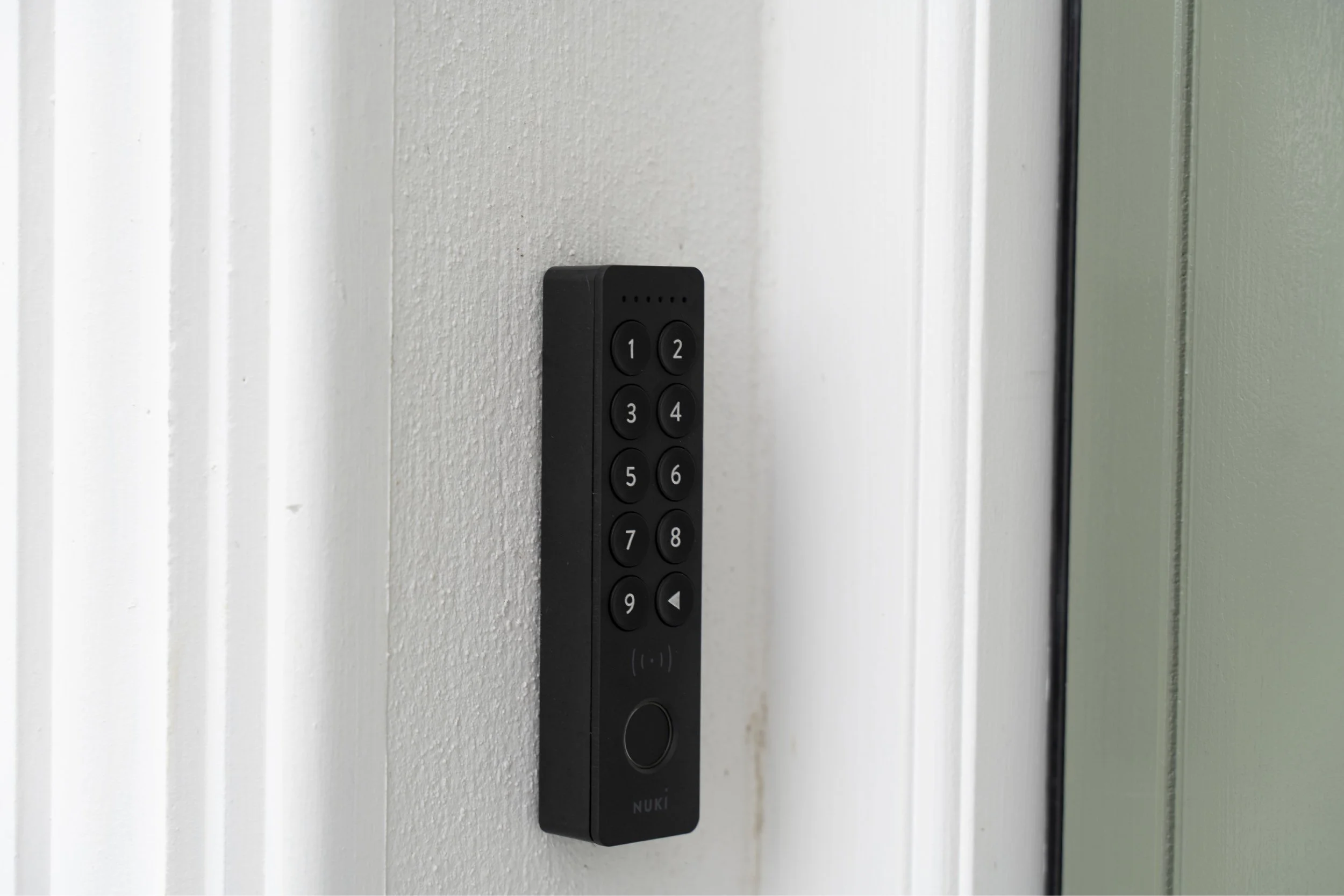 Close-up of a black remote control keypad with numbered buttons, mounted on a white wall near a door frame.