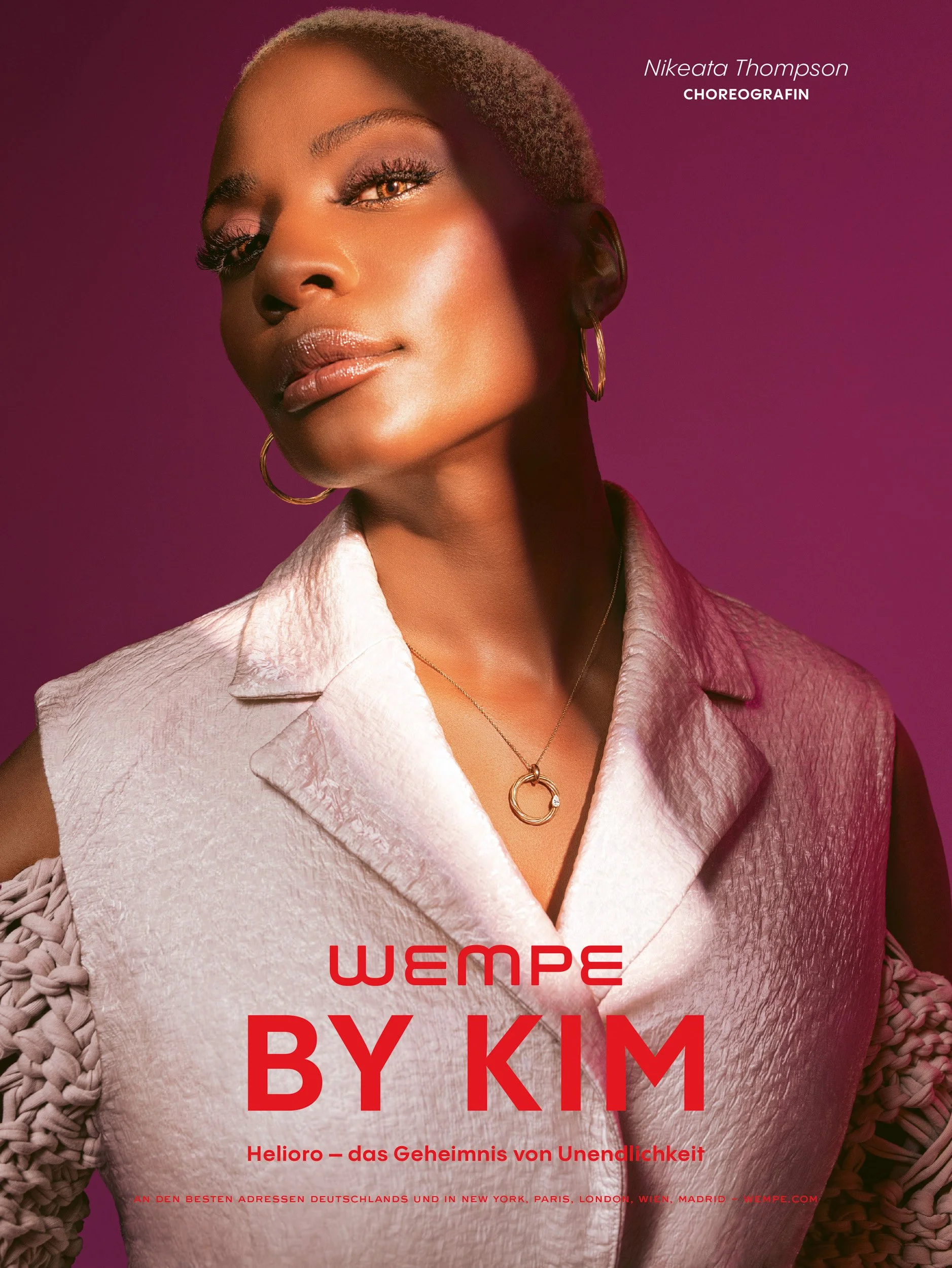 Close-up beauty portrait of a woman with short hair, gold hoop earrings, and a pendant necklace against a magenta background, with Wempe logo.