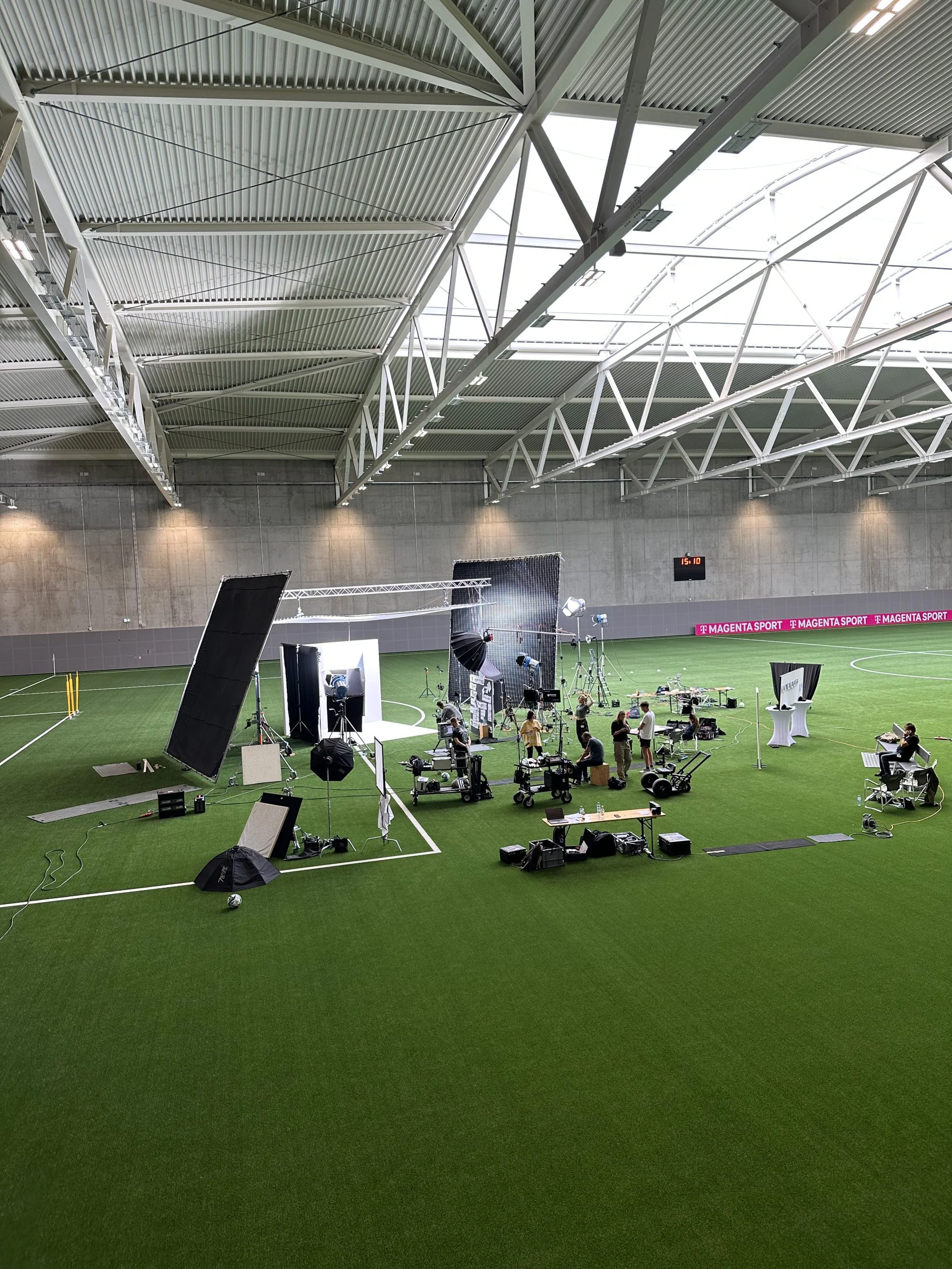 Wide view of an indoor sports hall set up for a photo shoot, with lighting rigs, backdrops, and a "T Magenta Sport" banner along the sideline.