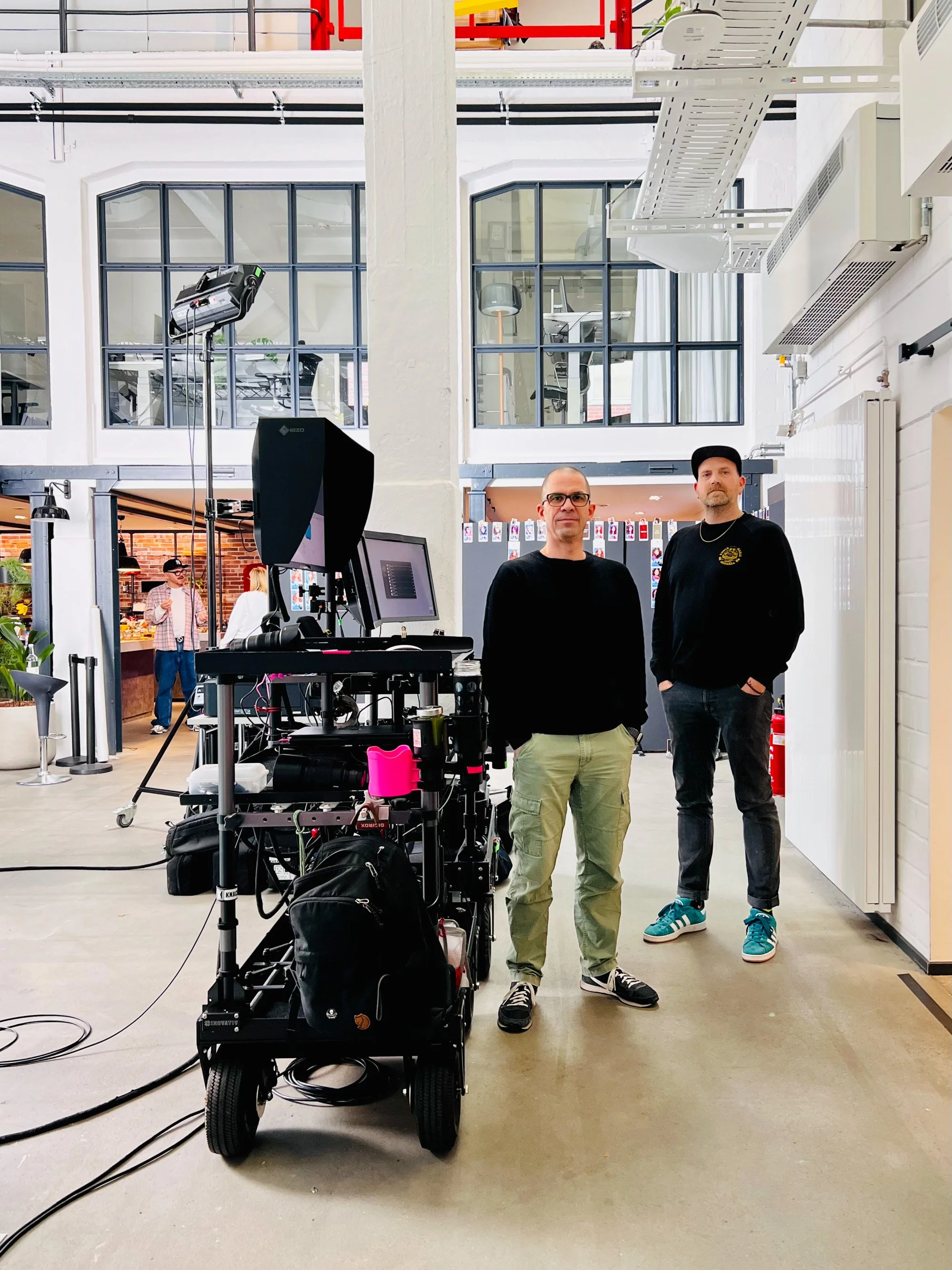 Two crew members standing beside a DIGIROX monitor cart in an industrial loft space with large windows.