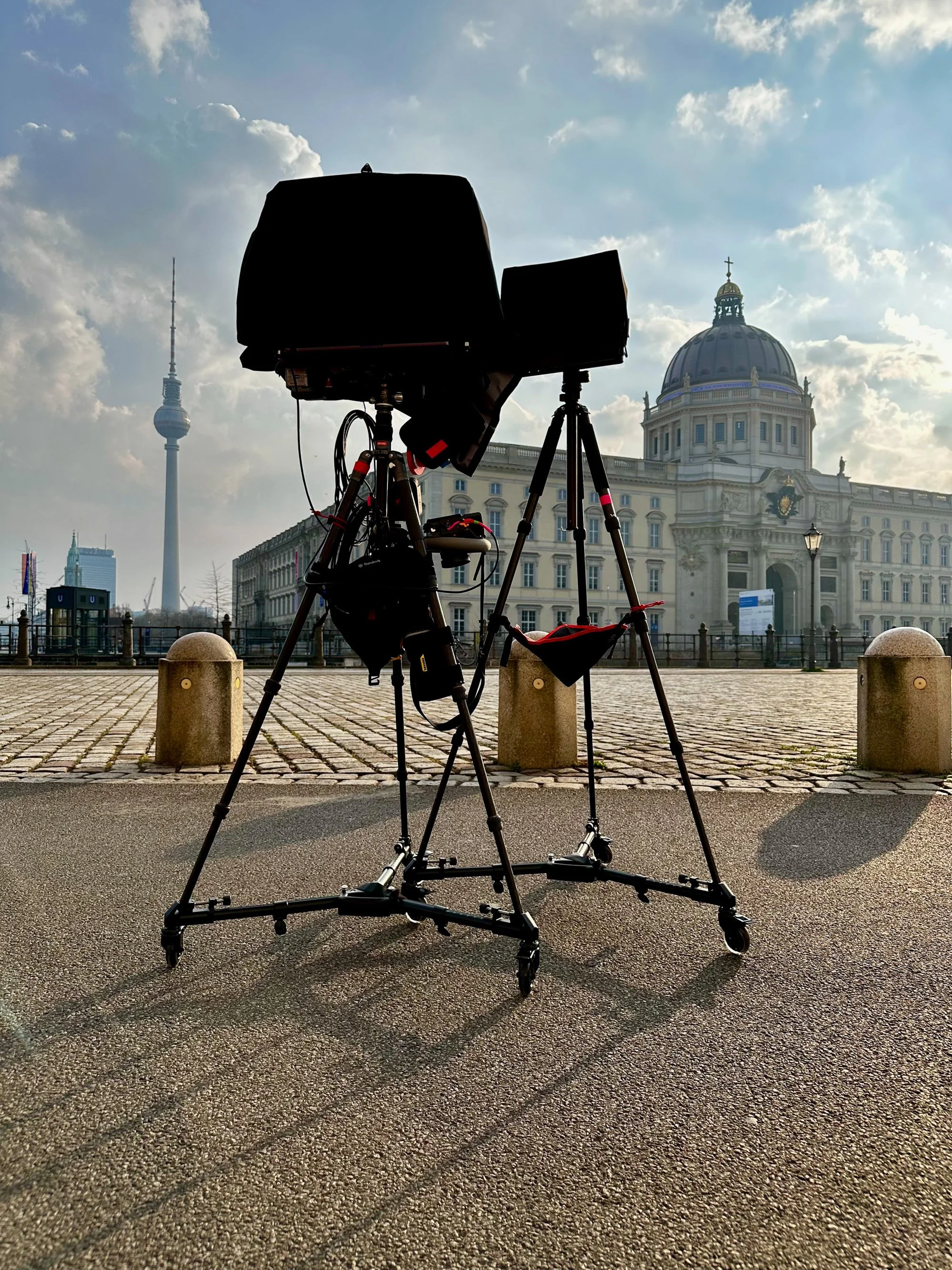 Hooded monitor on a tripod set up in an outdoor plaza, with the Berlin TV Tower and Berliner Schloss visible in the background.