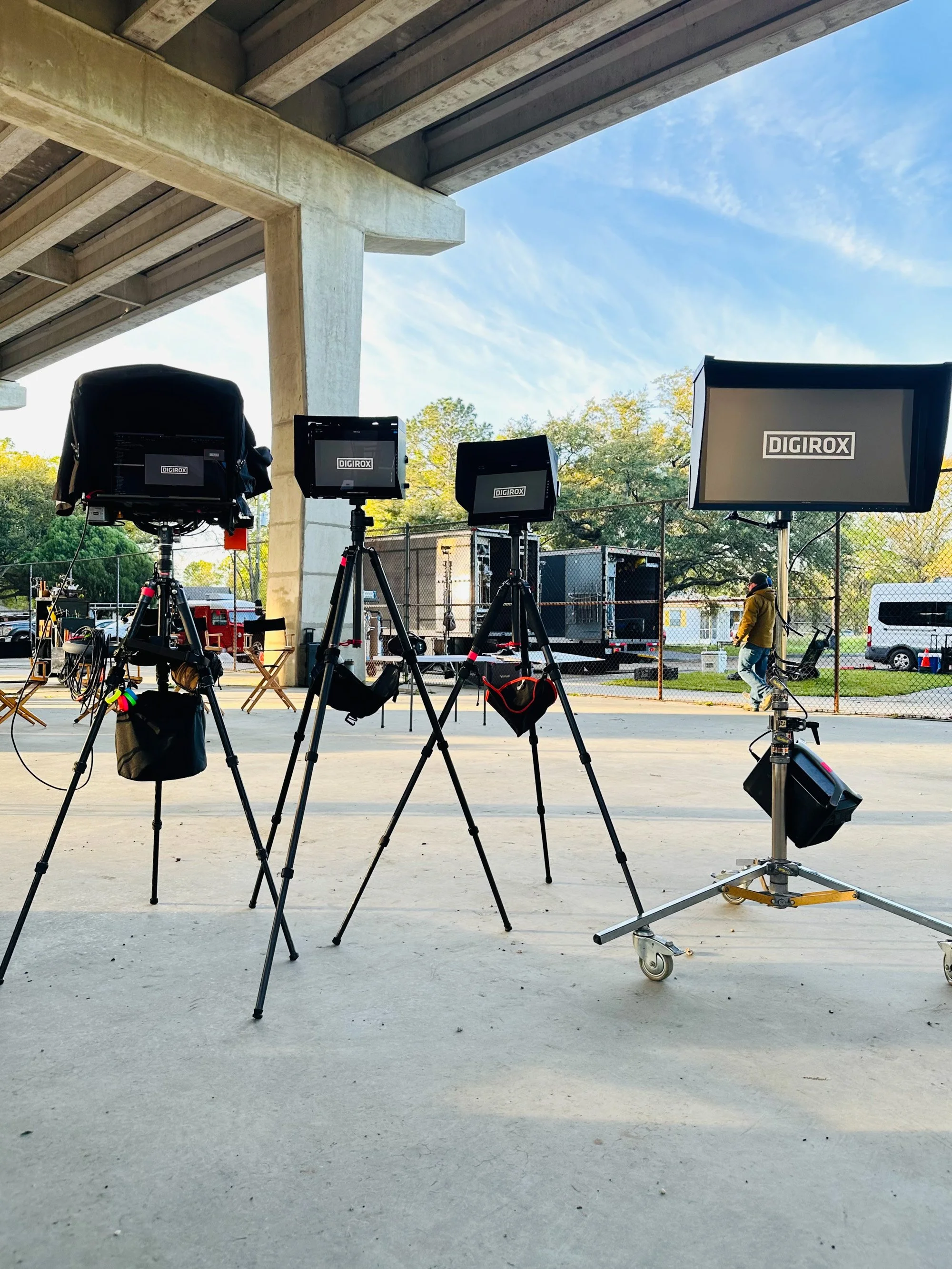 Four DIGIROX monitors on tripods set up under a covered outdoor structure, with trucks and a chain-link fence in the background.