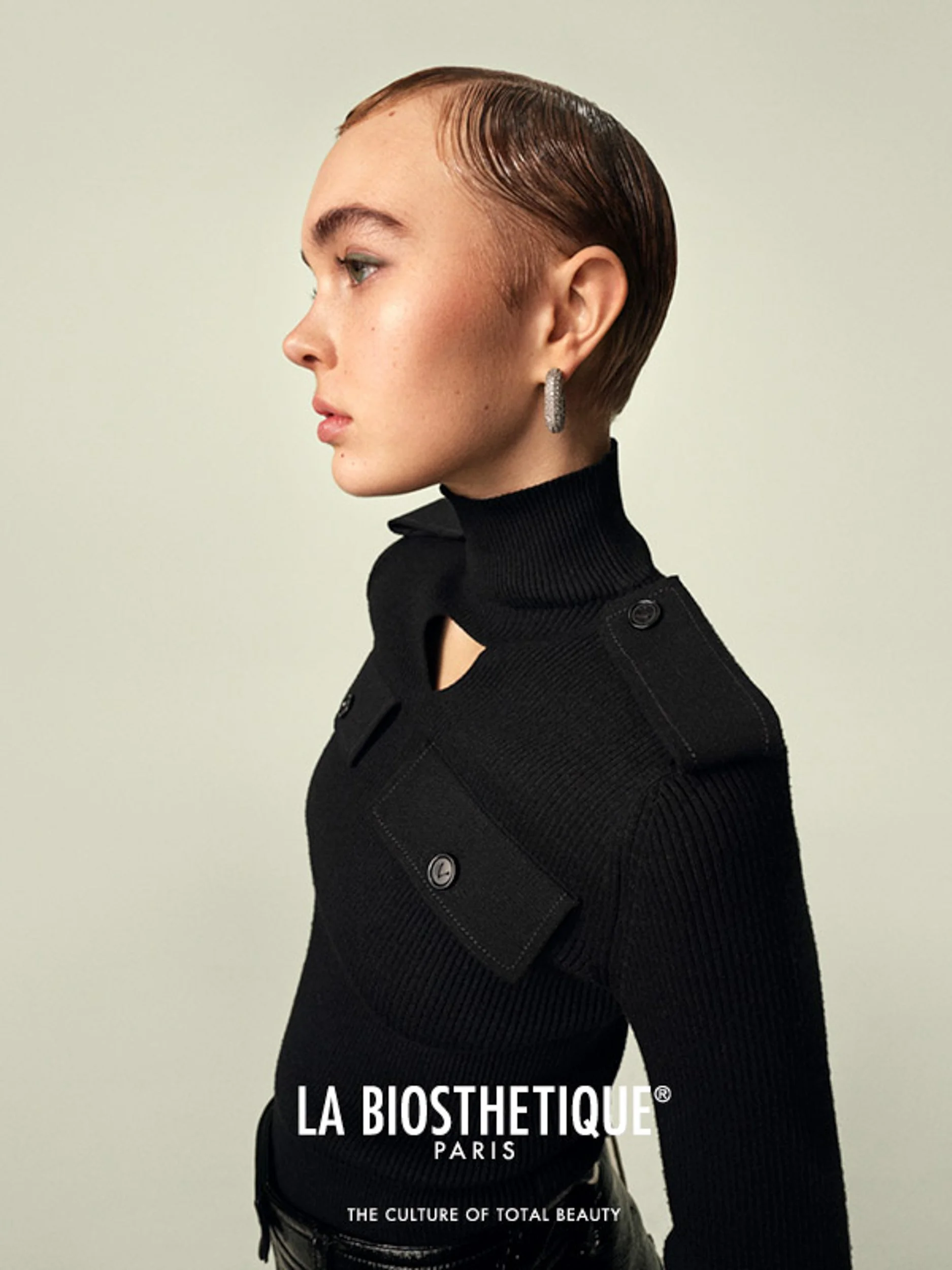 Profile portrait of a woman with slicked-back hair wearing a black ribbed turtleneck jacket, with La Biosthetique Paris logo.