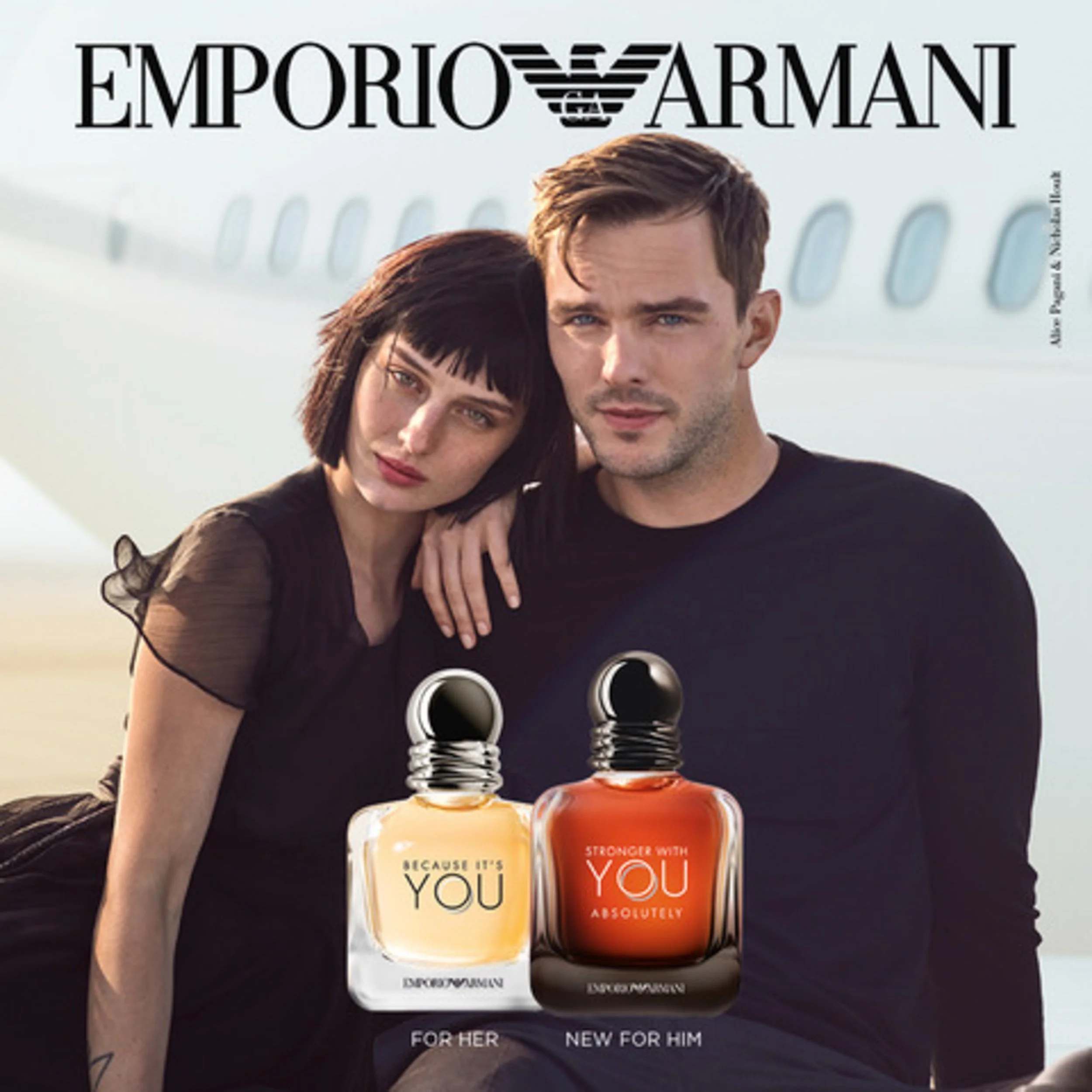 Couple in black outfits leaning together in front of a private jet, with two perfume bottles and Emporio Armani logo.