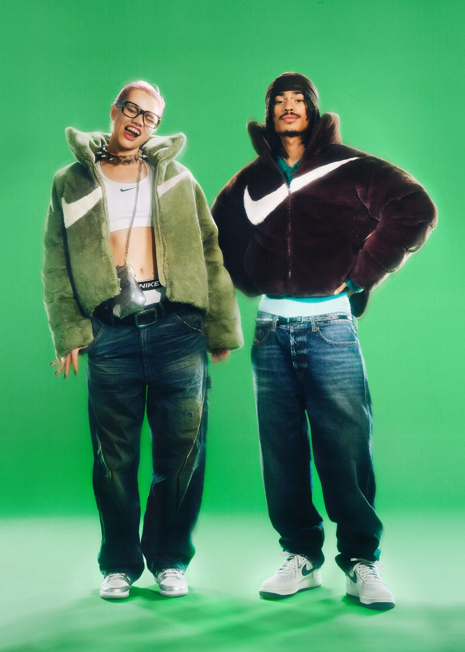 Two young models in oversized green and brown Nike faux-fur jackets and baggy jeans, posing against a bright green background.