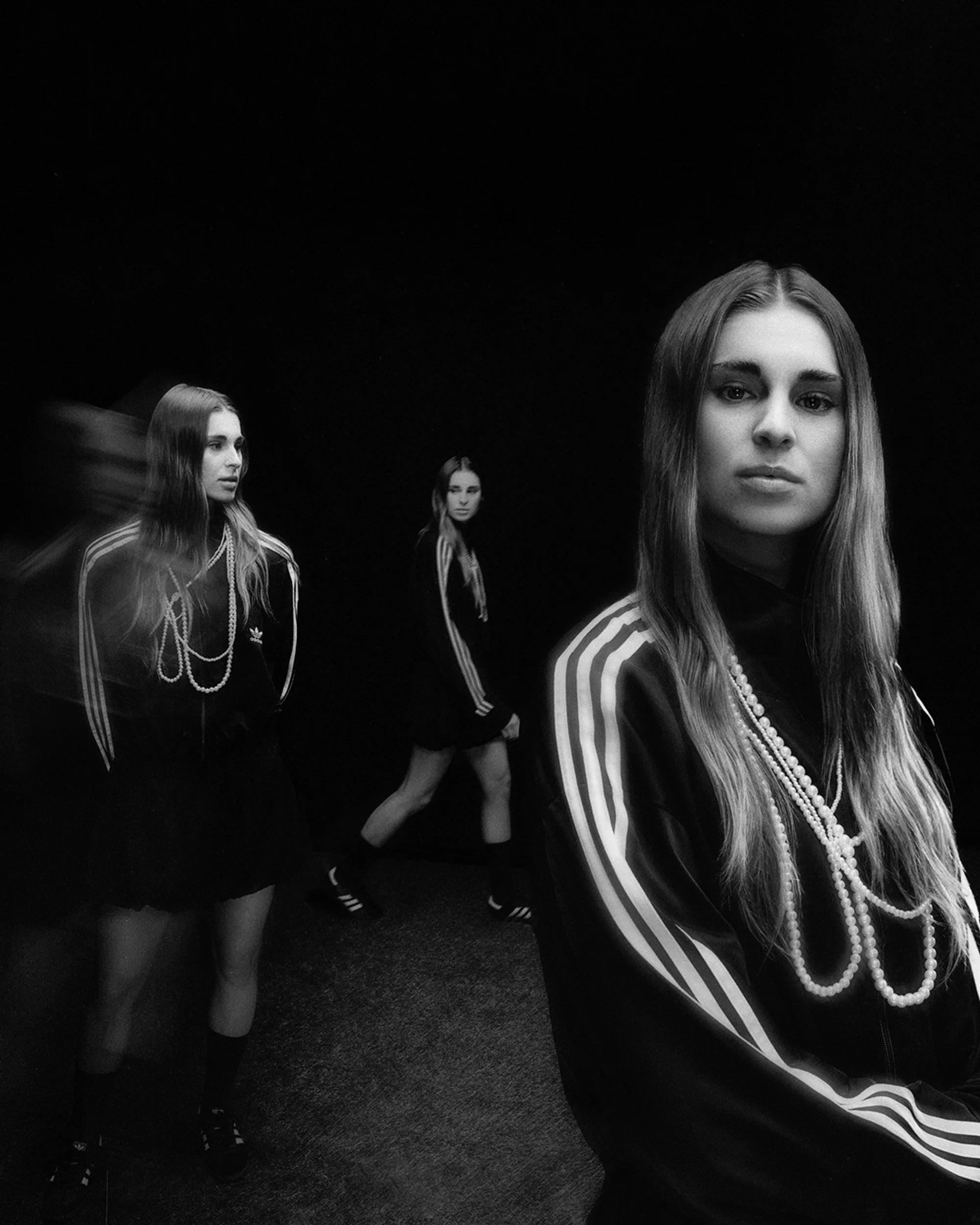 Black-and-white portrait series of a woman in an Adidas track jacket with pearl necklaces, shown in triple exposure against a dark background.