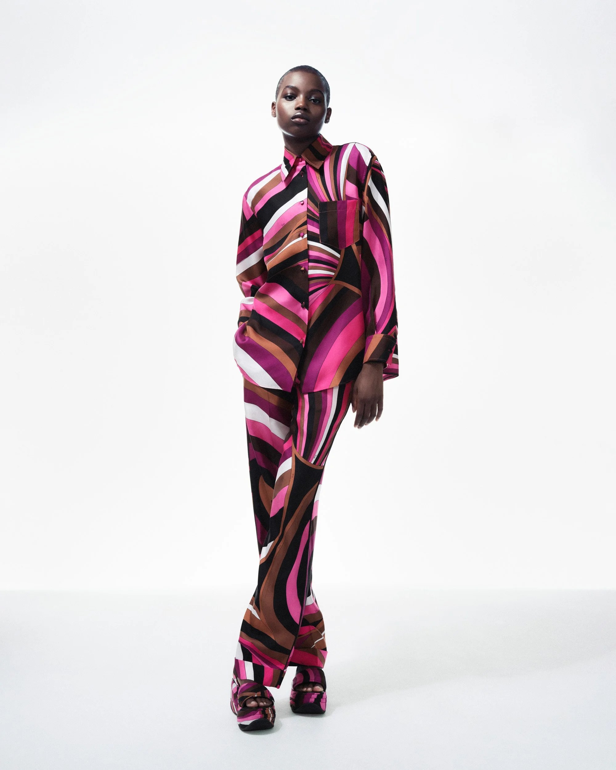 Model in a colorful pink, brown, and black swirl-print shirt and matching trousers, standing against a white backdrop.