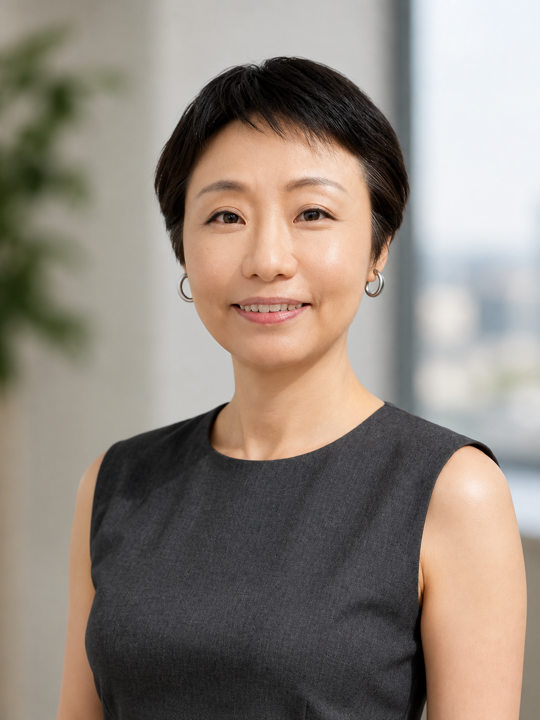 Smiling Asian woman with short dark hair and hoop earrings wearing a sleeveless black dress in an office