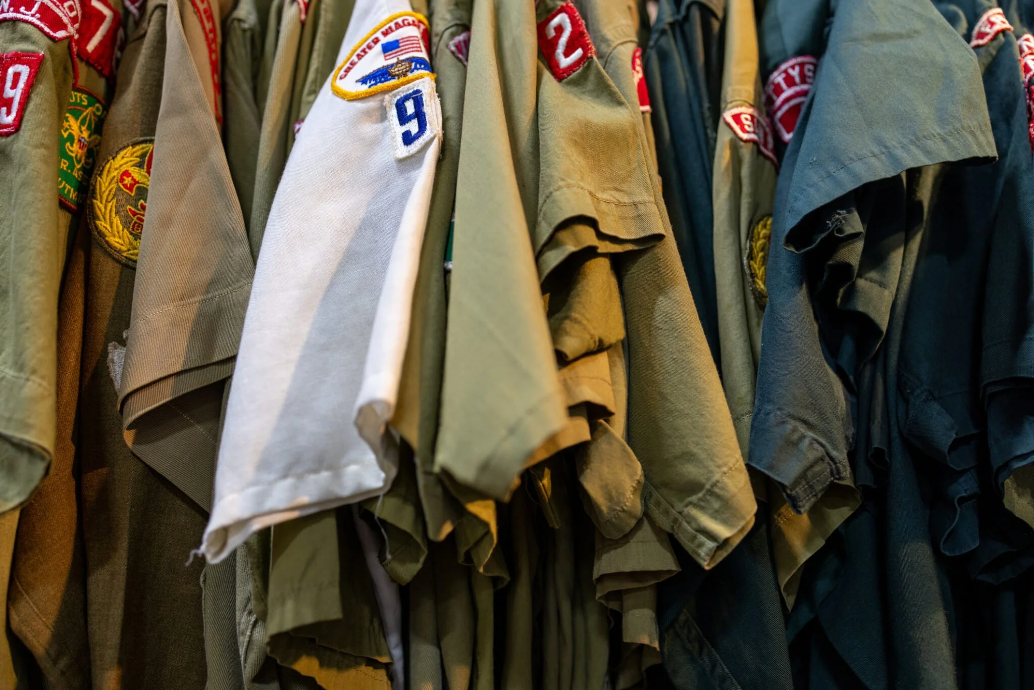 A row of military-style jackets or shirts hanging on a rack, featuring various patches and badges.