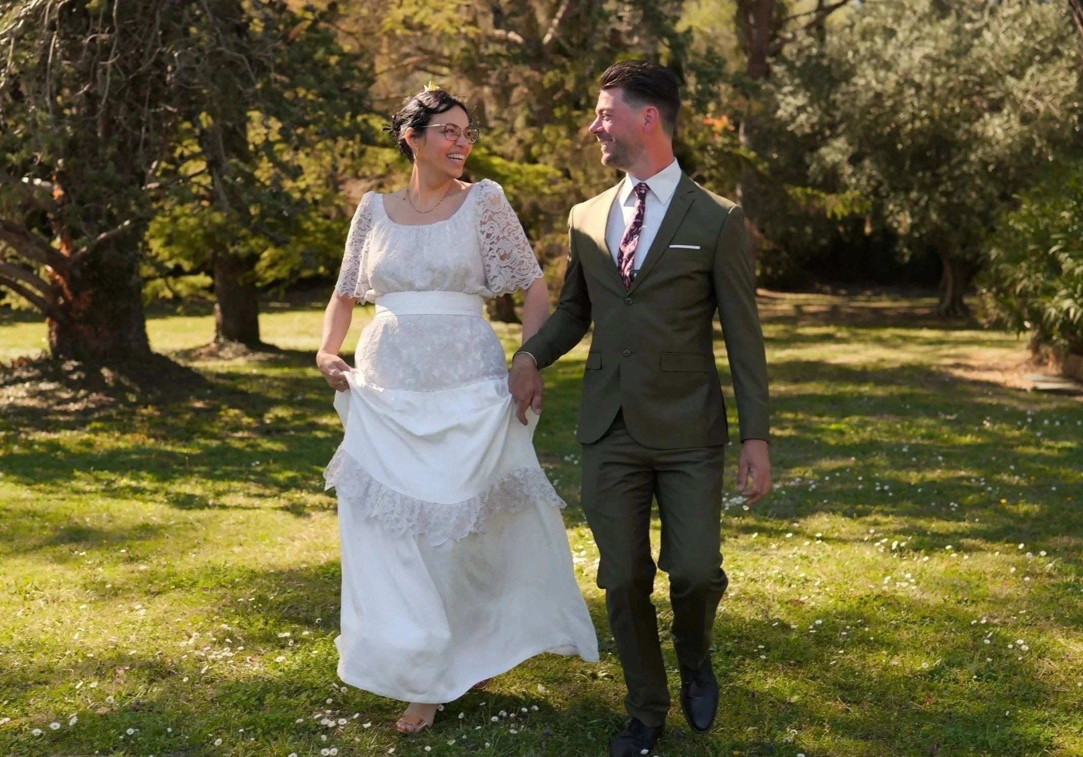Deux personnes en tenue de mariage marchent dans un parc en automne, s'embrassant et souriant.