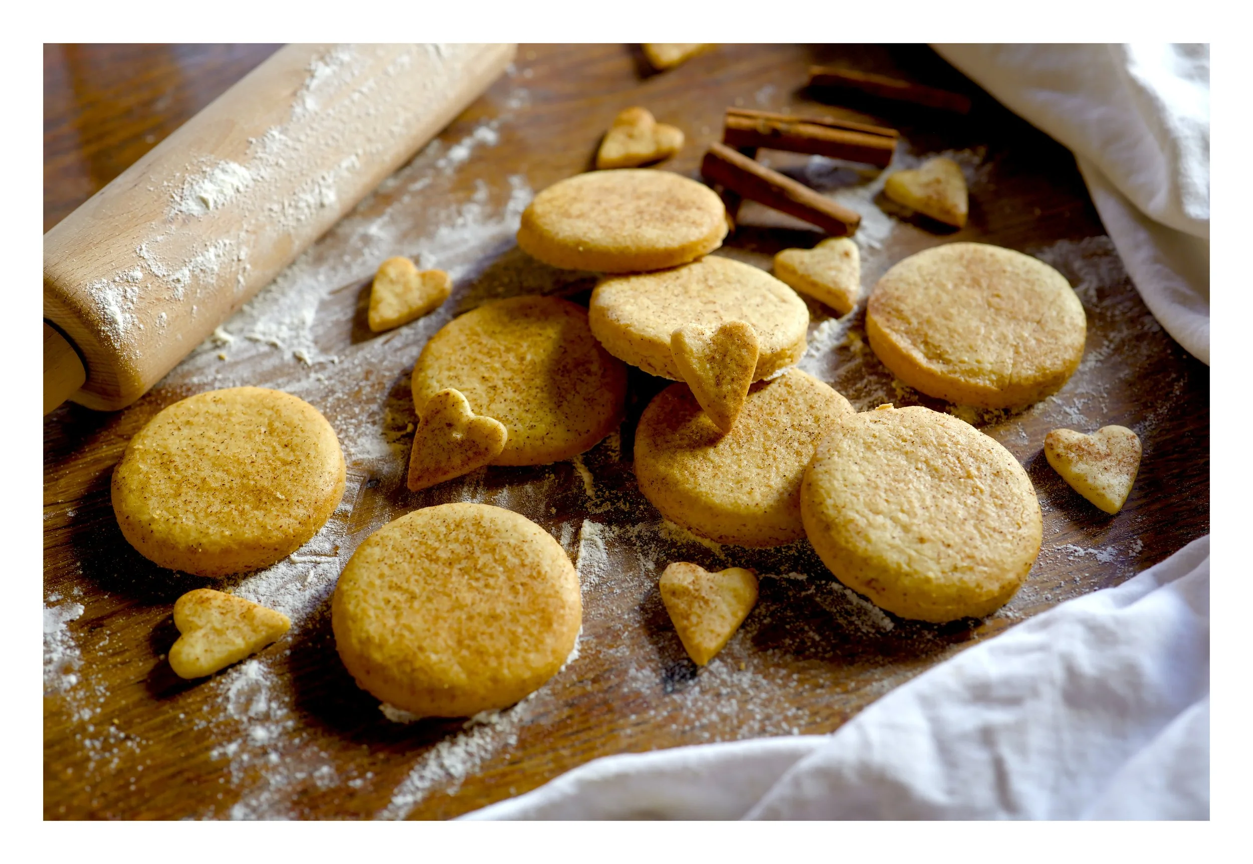 Pâtisserie en cours de préparation avec biscuits ou sablés en forme de cœurs, ronds et autres formes, saupoudrés de farine, sur une surface en bois avec un rouleau à pâtisserie.