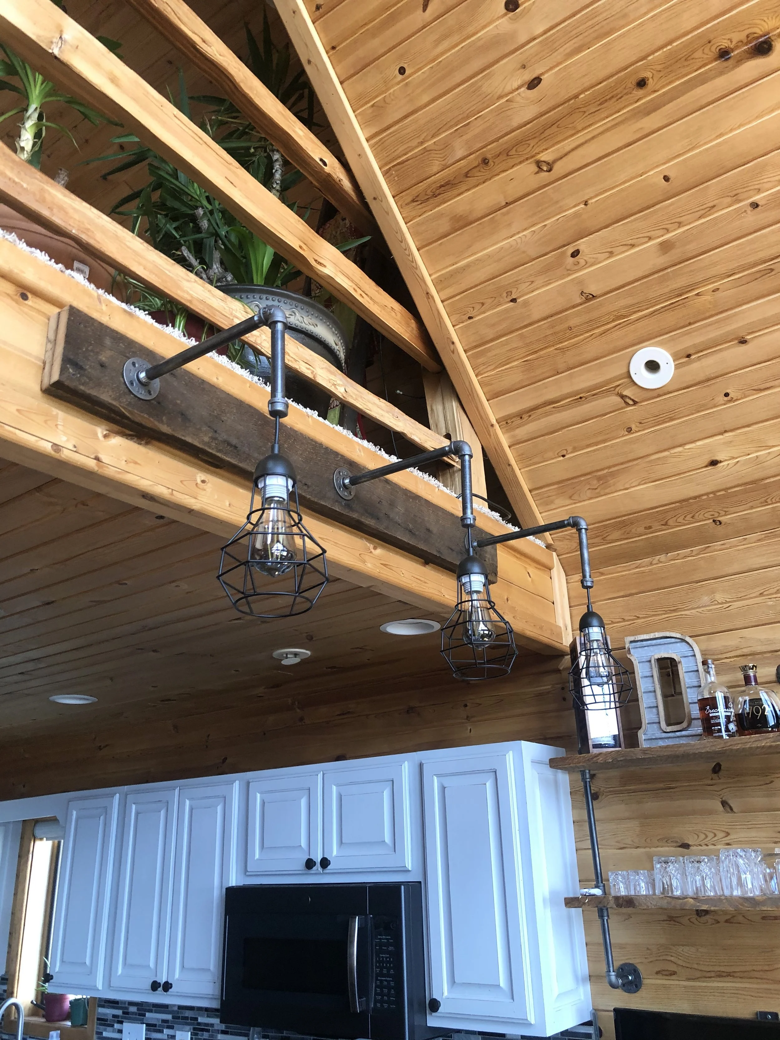 Interior view of a kitchen with a wooden ceiling, hanging industrial-style light fixtures, white cabinets, and a black microwave oven.