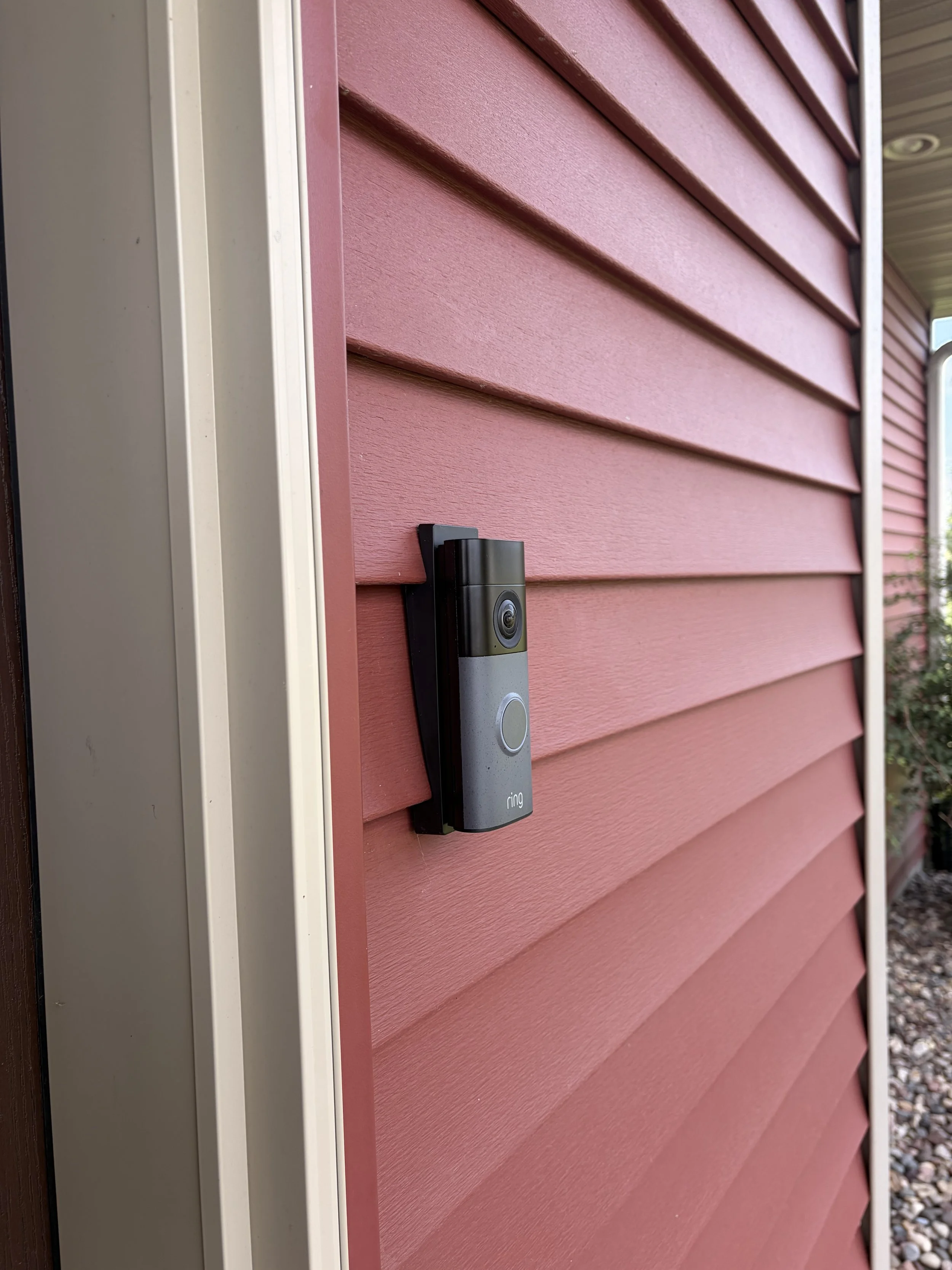 A close-up of a Ring video doorbell mounted on a pink house with horizontal siding.
