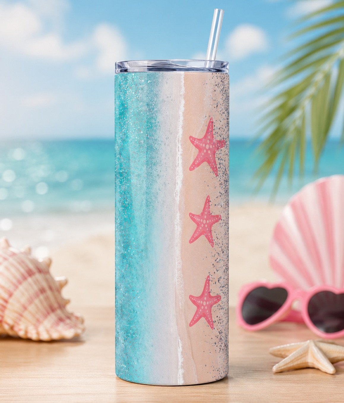 A tumbler with a beach scene design featuring starfish, placed on a wooden surface with seashells, pink sunglasses, and palm leaves in the background near the ocean.
