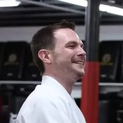 Ryan M., a parent and student, smiling on the mat in his gi