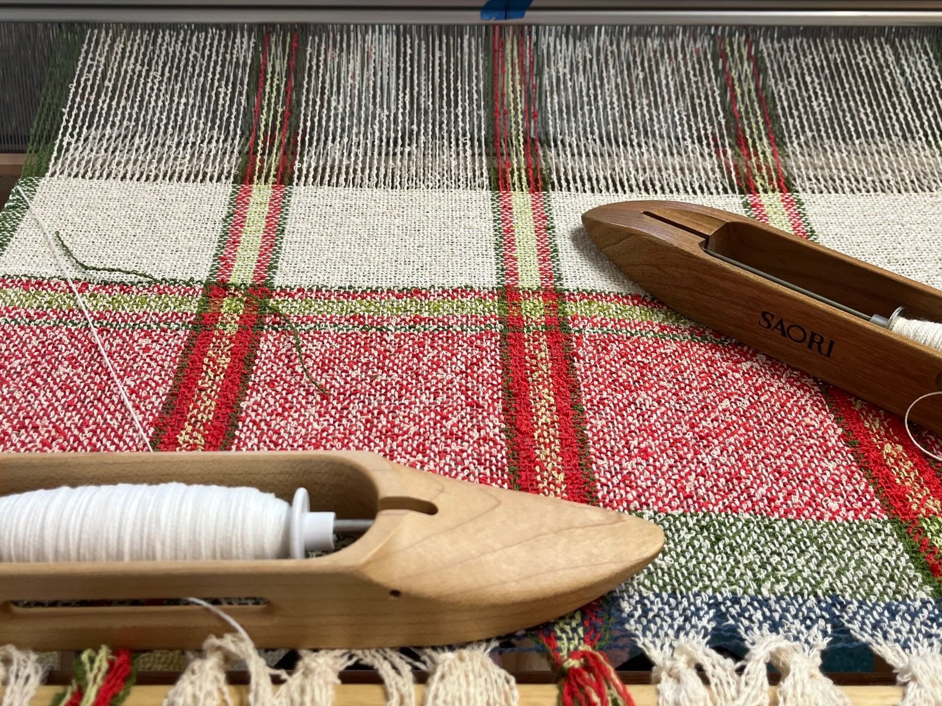A weaving loom and colorful woven fabric with red, green, white, and blue patterns.