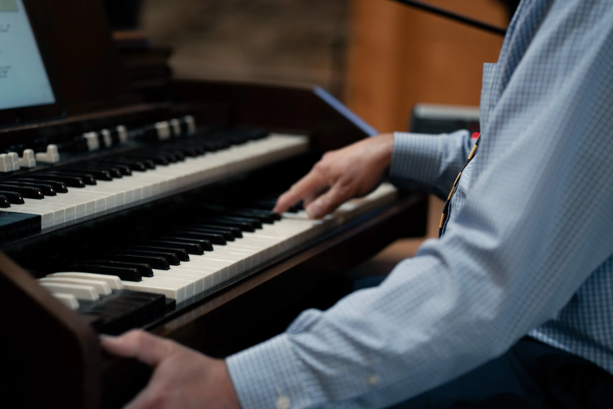 A person in a blue checkered shirt playing a black upright piano.