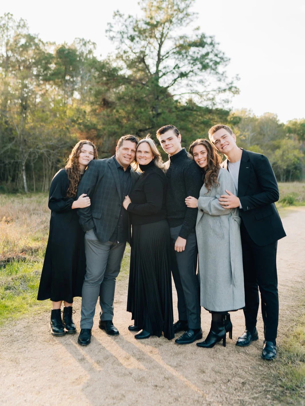 A family of six standing outdoors in a park during autumn, smiling and hugging each other.