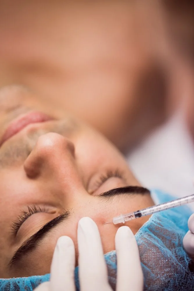 Paciente recebendo aplicação de injeção na testa por profissional de saúde com luvas e máscara, em ambiente clínico.